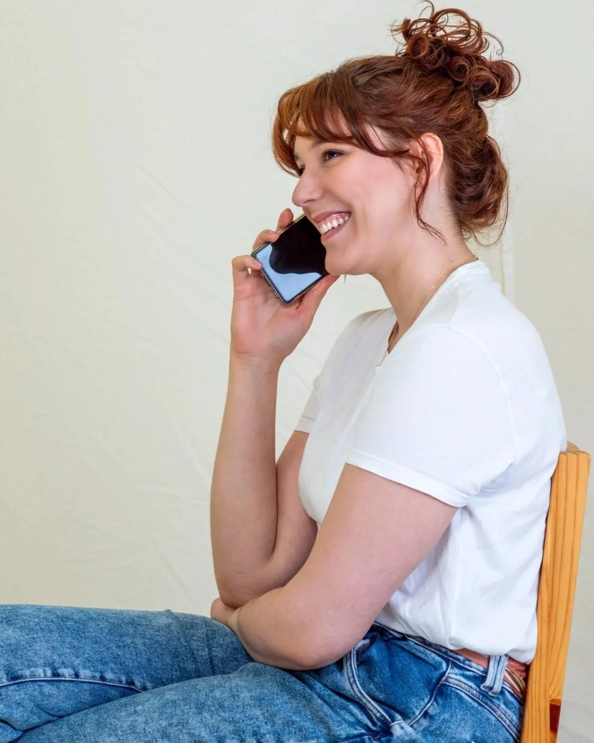 A woman with curly red hair smiling while talking on a cellphone.