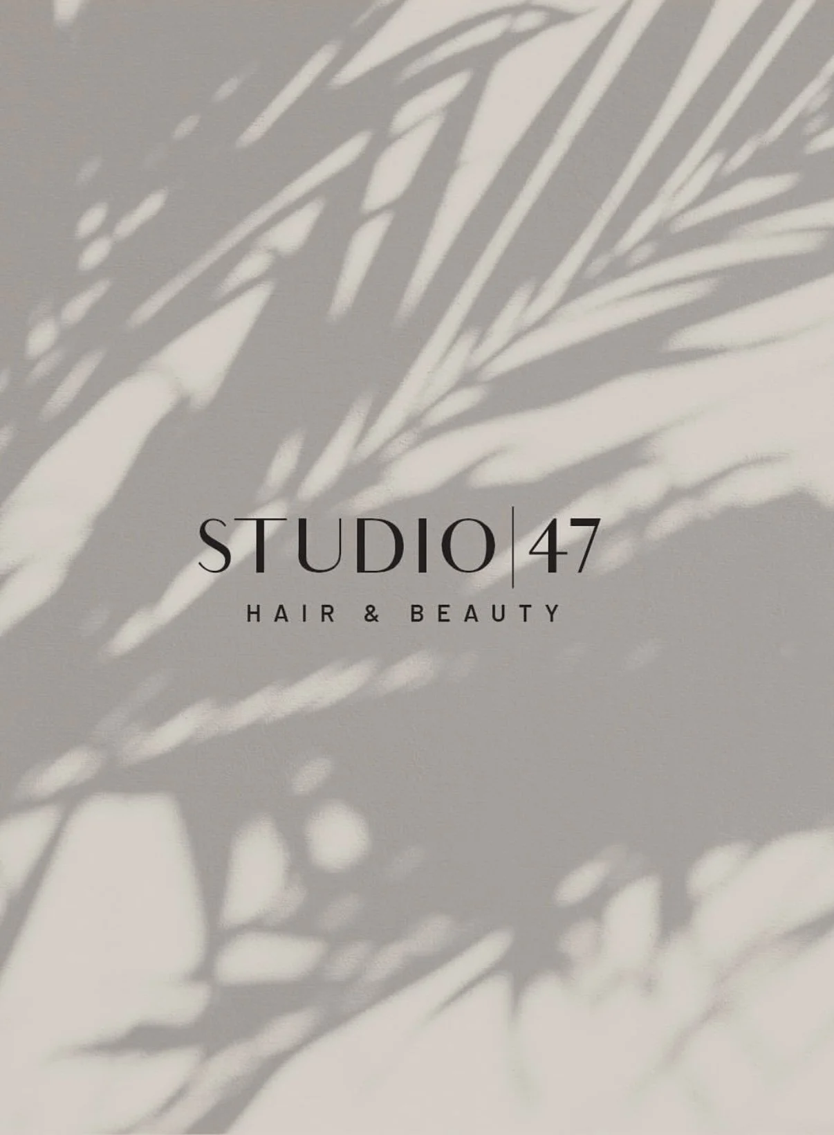 A sign for Studio 47 Hair & Beauty with shadows of leaves cast on the wall behind it.
