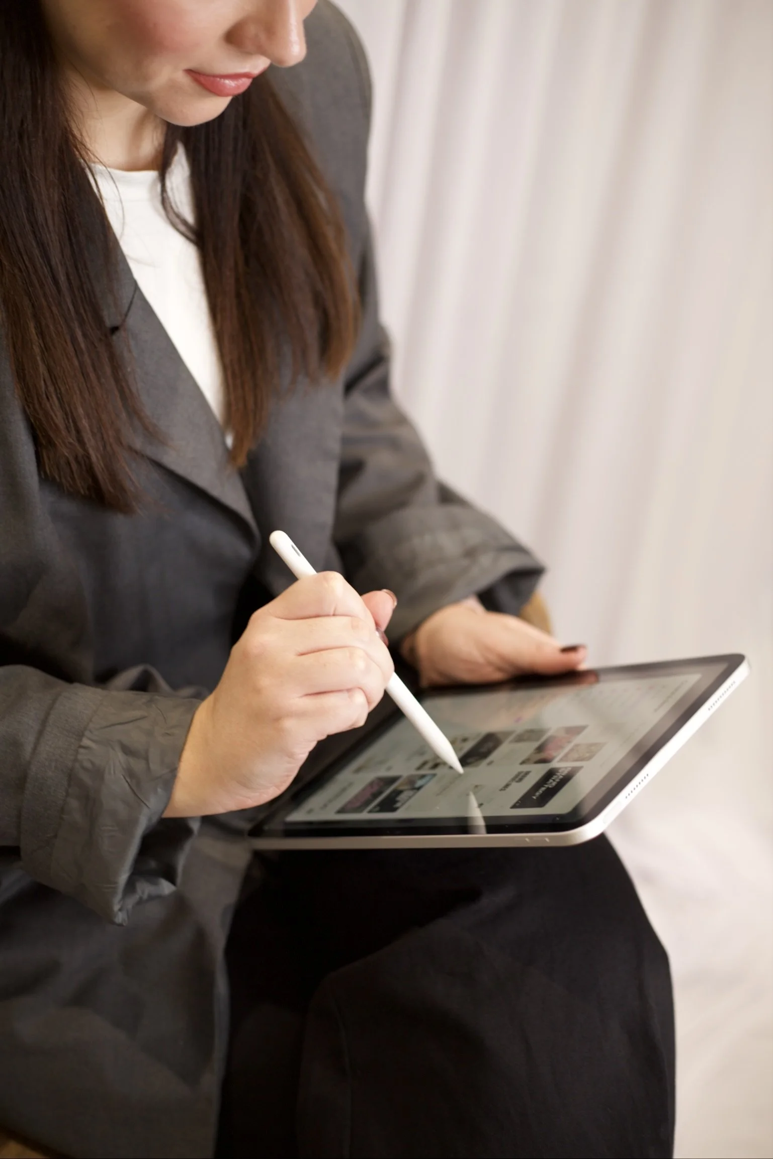 A woman sitting down, using a stylus to navigate a tablet device.