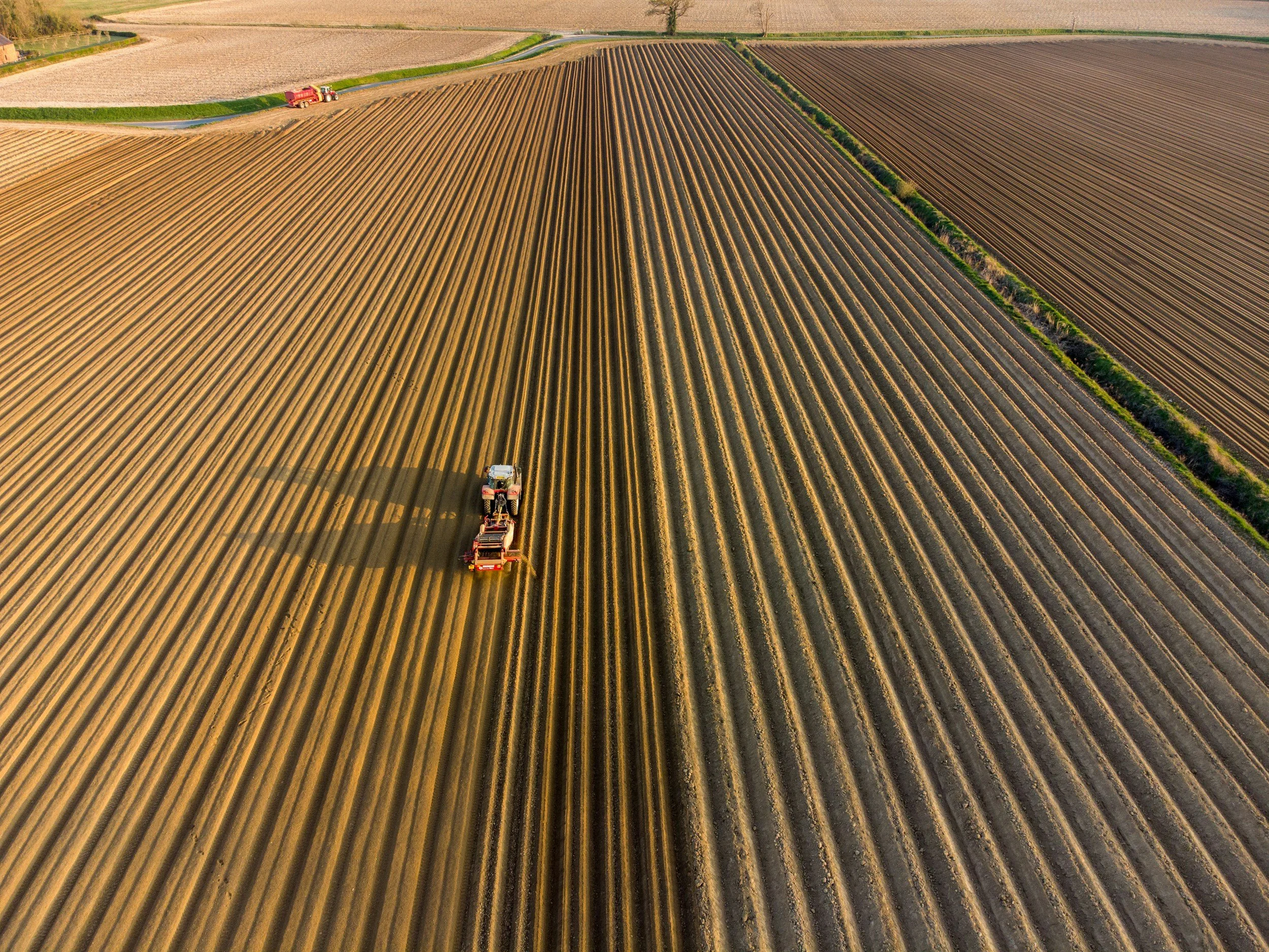 Luftaufnahme eines landwirtschaftlichen Feldes mit Traktor, das den Boden pflügt.
