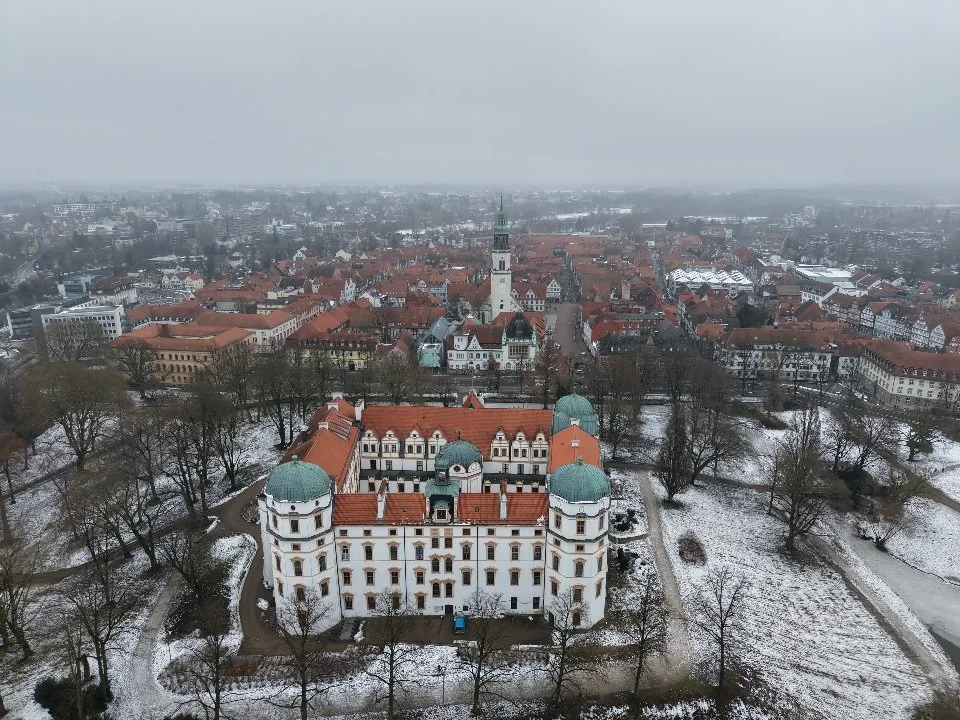 Luftaufnahme einer historischen Stadt mit einer Burg im Vordergrund, umgeben von Bäumen und Straßen, im Winter mit Schneedecke. Celle Winter. Stadt Celle Drohnenaufnahme