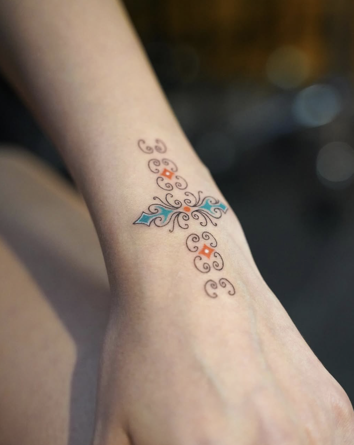Colorful tattoo on a person's forearm with swirls, diamonds, and small orange details.