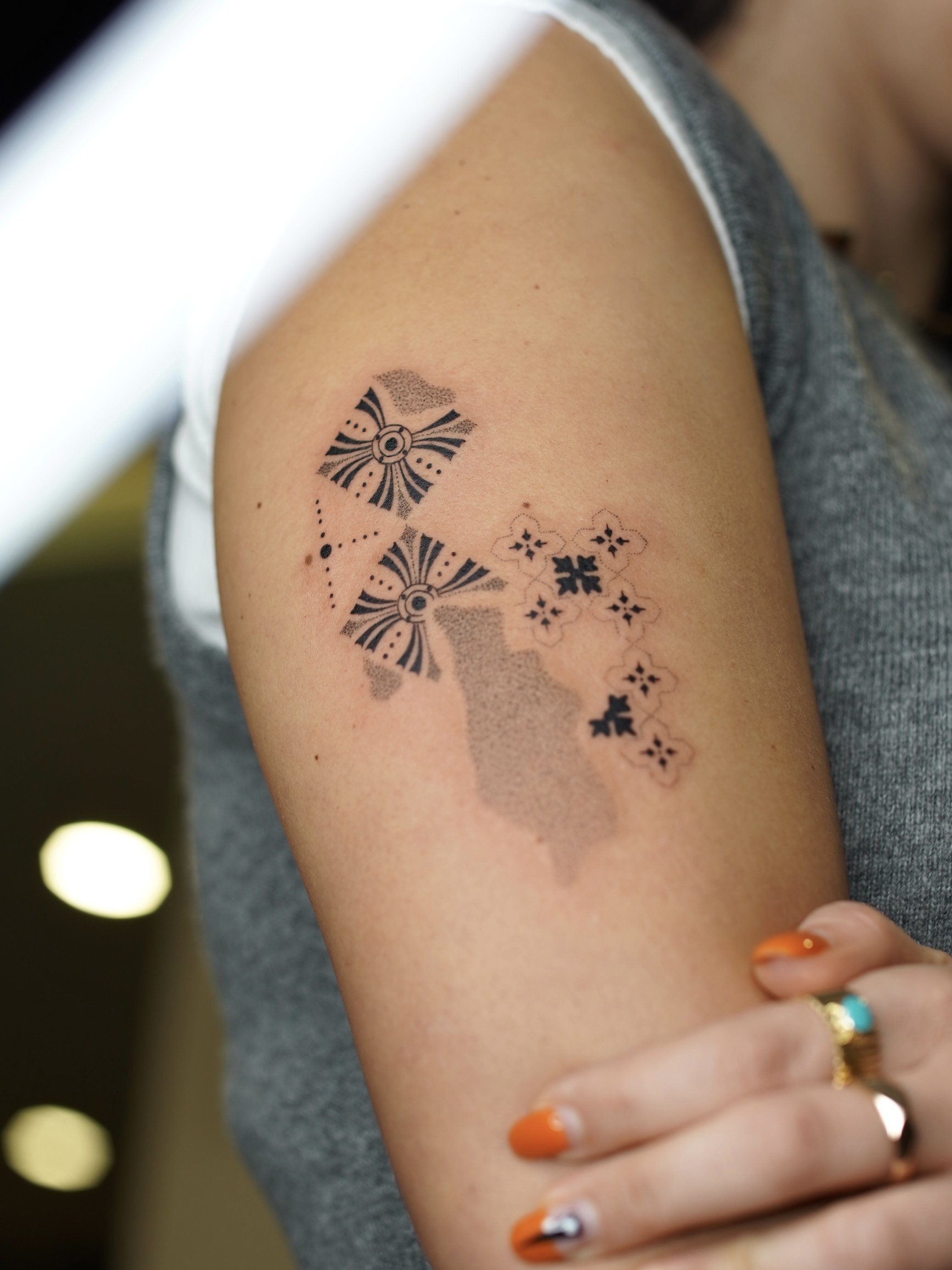 Tattoo of the map of California with decorative geometric patterns and floral motifs on a person's upper arm.