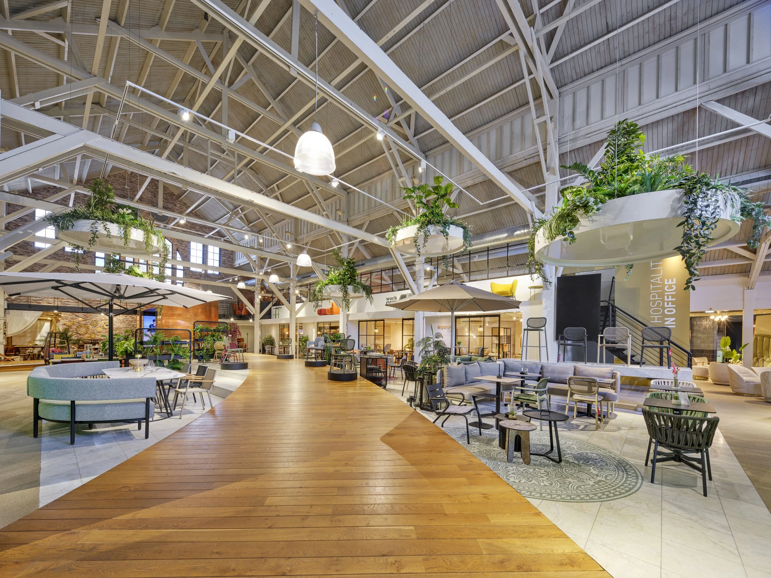 interior of a modern restaurant or lounge with high ceilings, lots of plants and seating areas, parasols, and wooden flooring