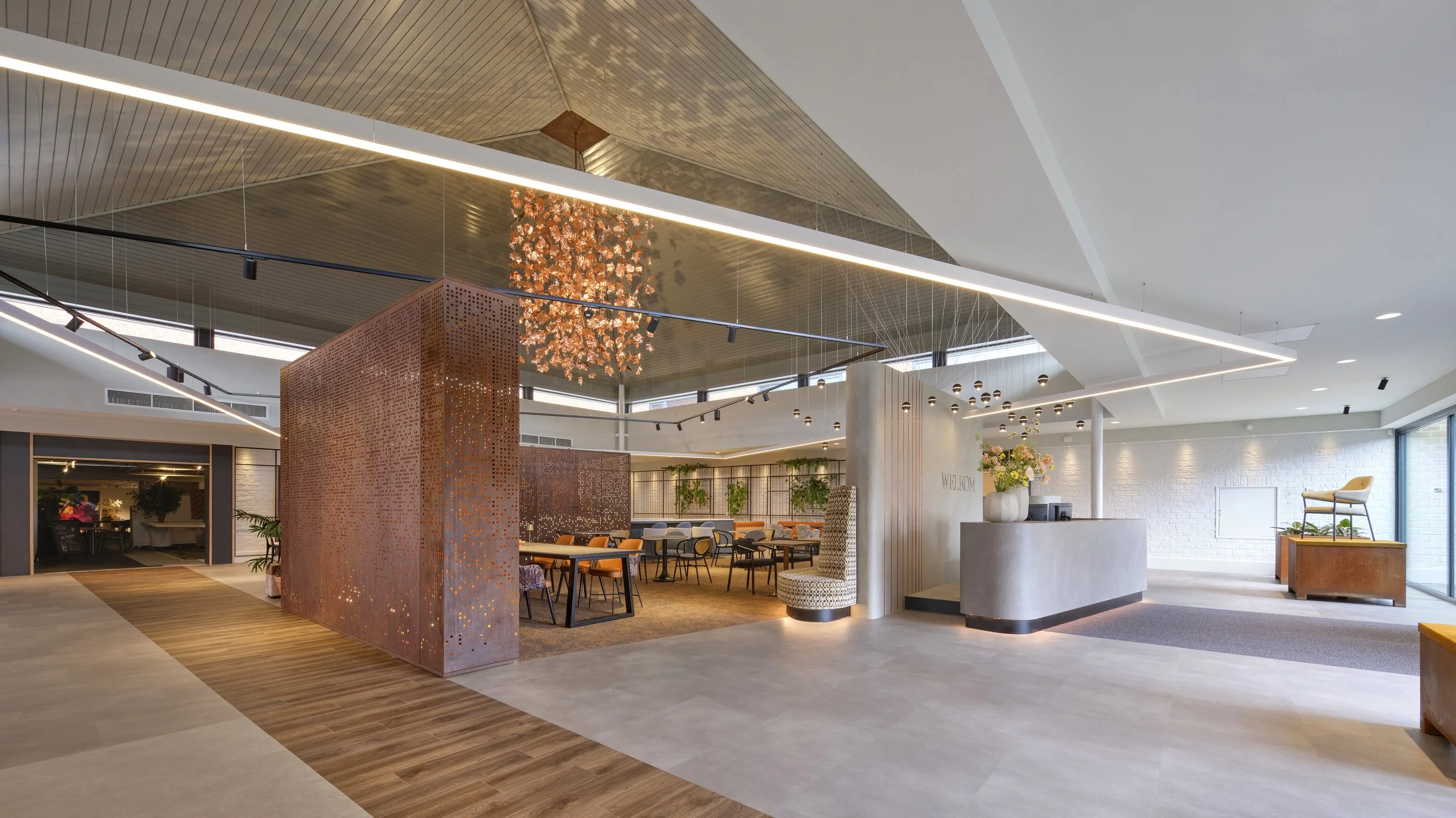 A modern hotel reception area with white/light-colored walls, a counter, and a seating area with chairs and plants.