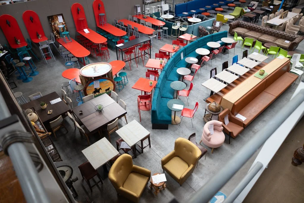 A colorful café with various seating options including tables, chairs, a long bench, a round bar, and a few armchairs, all in a modern and cozy interior.