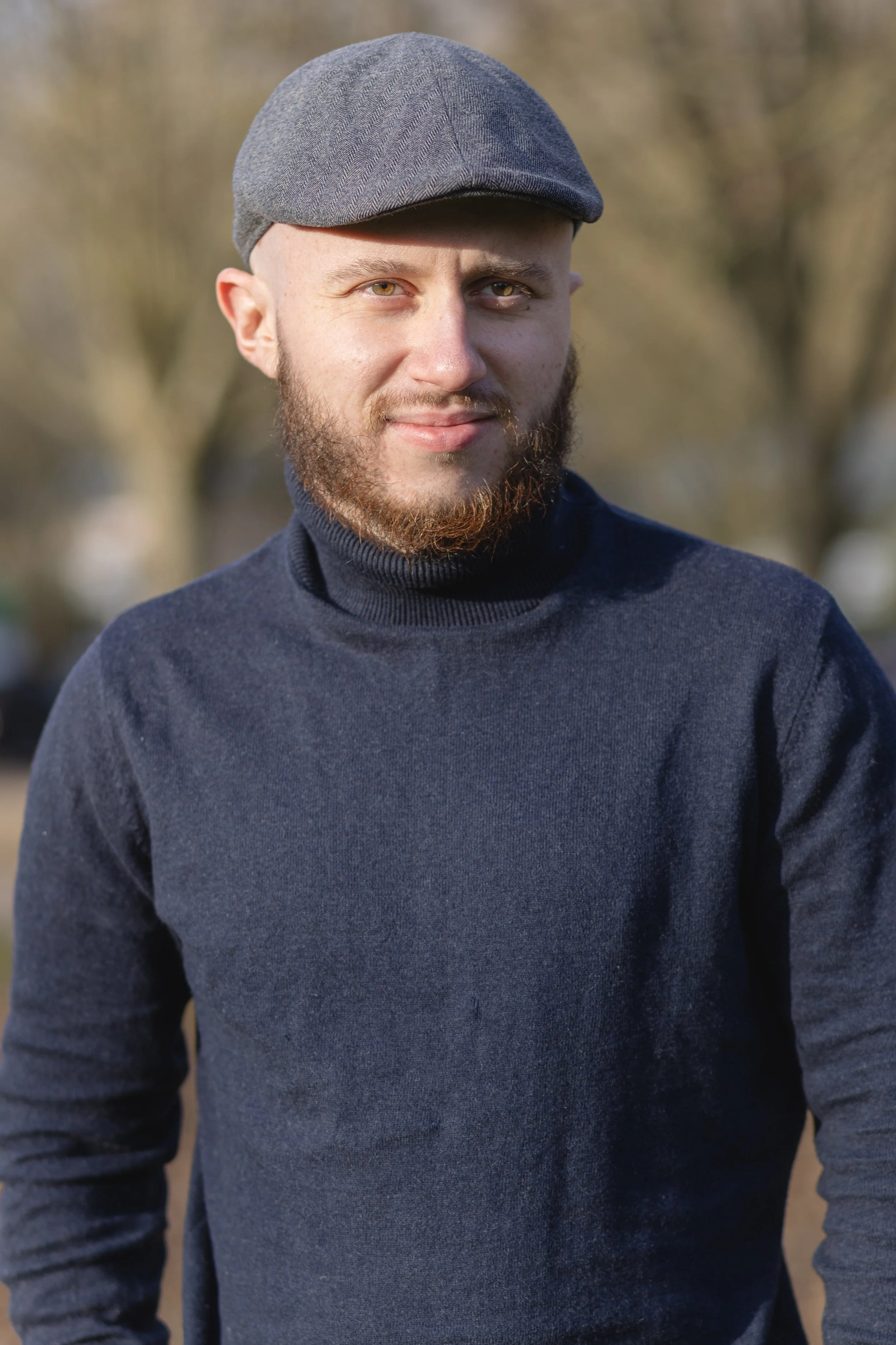 Le photographe Thomas Beuvin portant un béret gris et un pull bleu foncé, souriant, en plein air avec des arbres en arrière-plan.