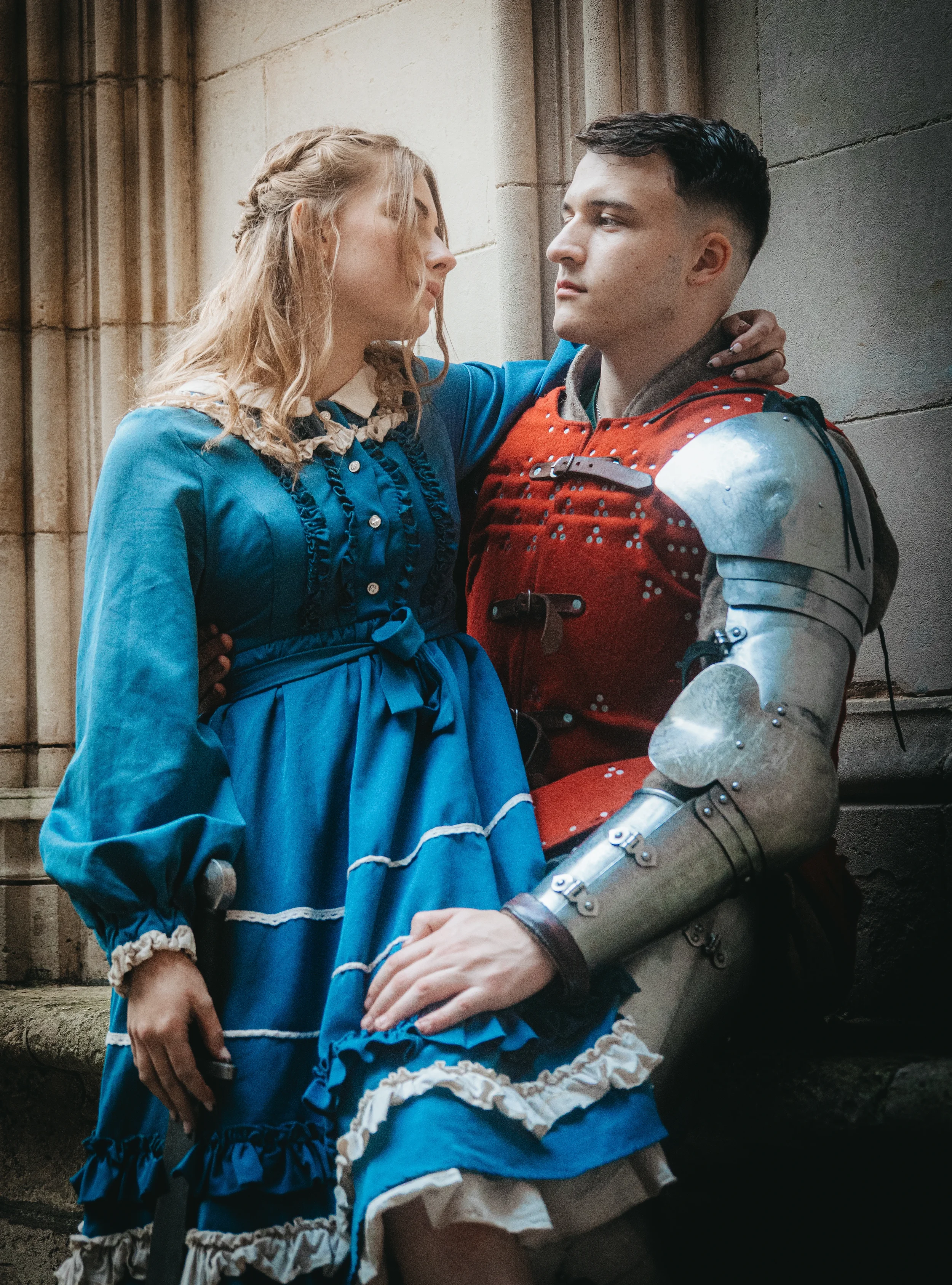 Une femme en robe bleue et un homme en armure de chevalier sont assis contre un mur.