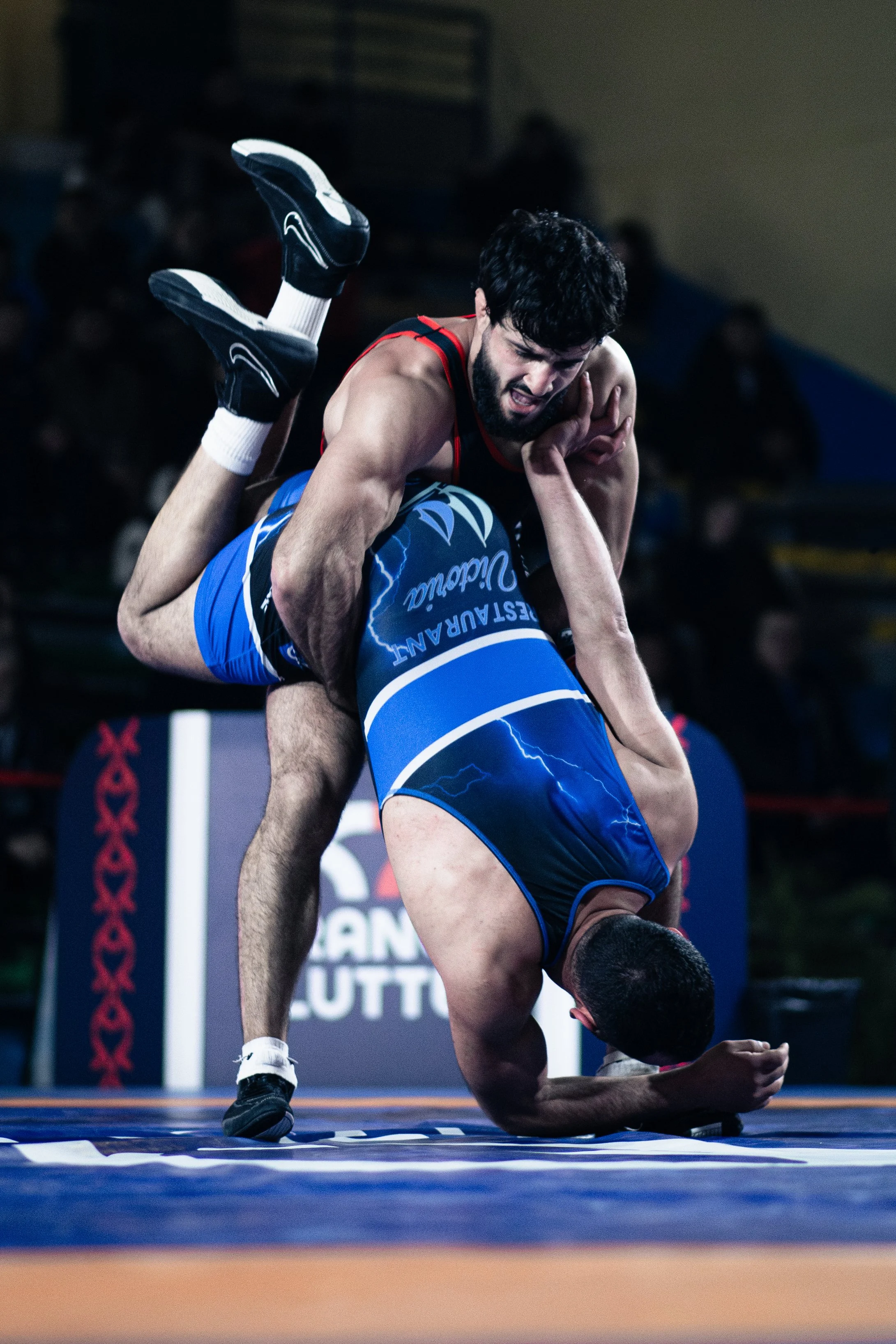 Deux lutteurs en plein combat durant un match de lutte gréco-romaine, un homme en position de prise au sol, l'autre en haut, en train de le soulever.