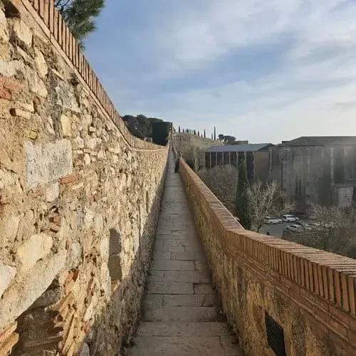 Rempart étroit entouré de murs en pierre et en brique montant en pente, avec des arbres et bâtiments anciens au fond, en plein jour, Remparts de Gérone, Espagne