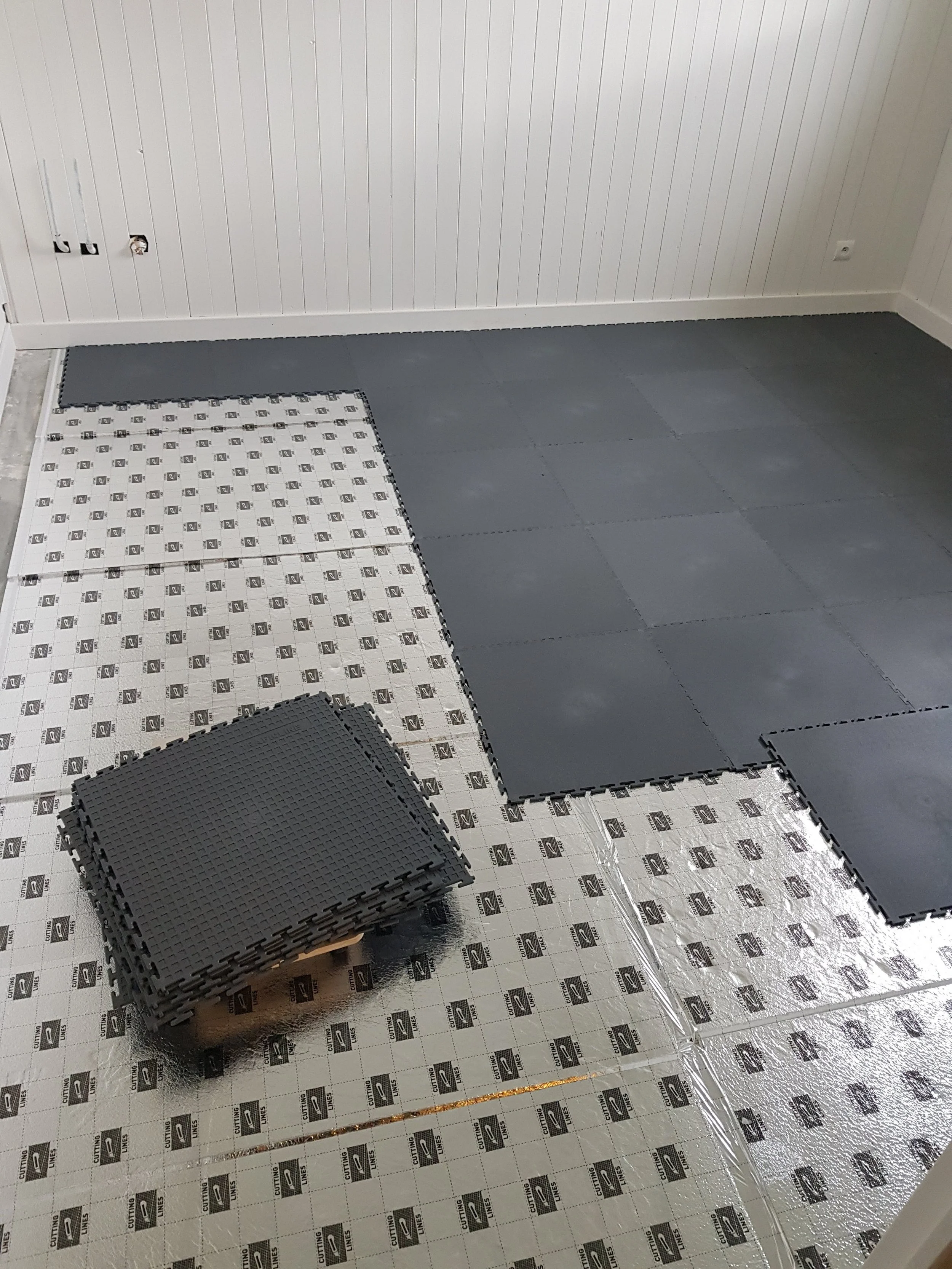 Pose de dalles en caoutchouc gris pour un revêtement de sol, avec des dalles en place partiellement.