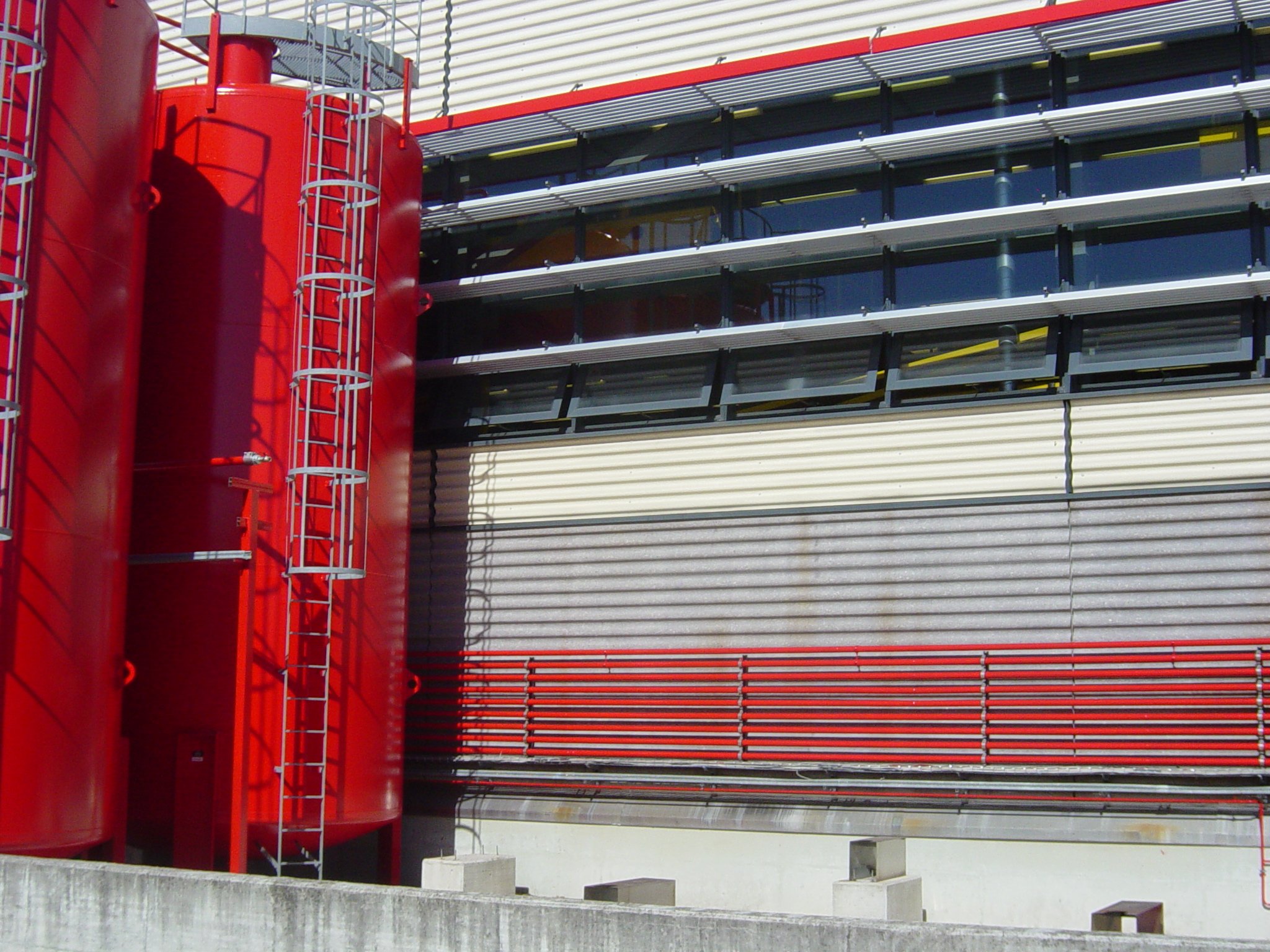 Structures architecturales modernes avec toits en métal et éléments en acier, principalement rouges, gris, et noirs, avec des escaliers et des plateformes.