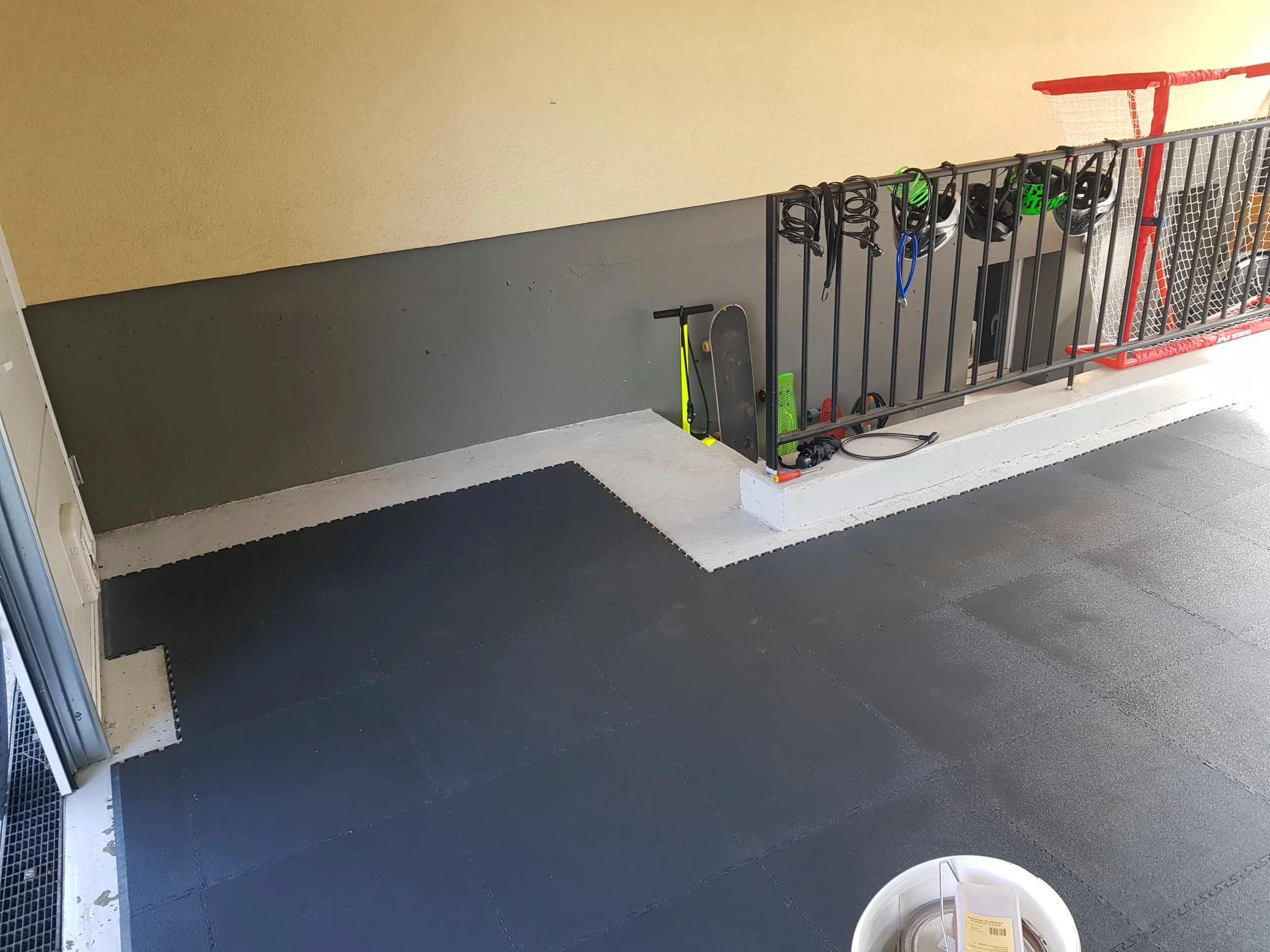 Espace pour ranger des équipements de sport, avec un skate et un vélo fauteuil, casques, et barrières de sécurité, dans un environnement intérieur.