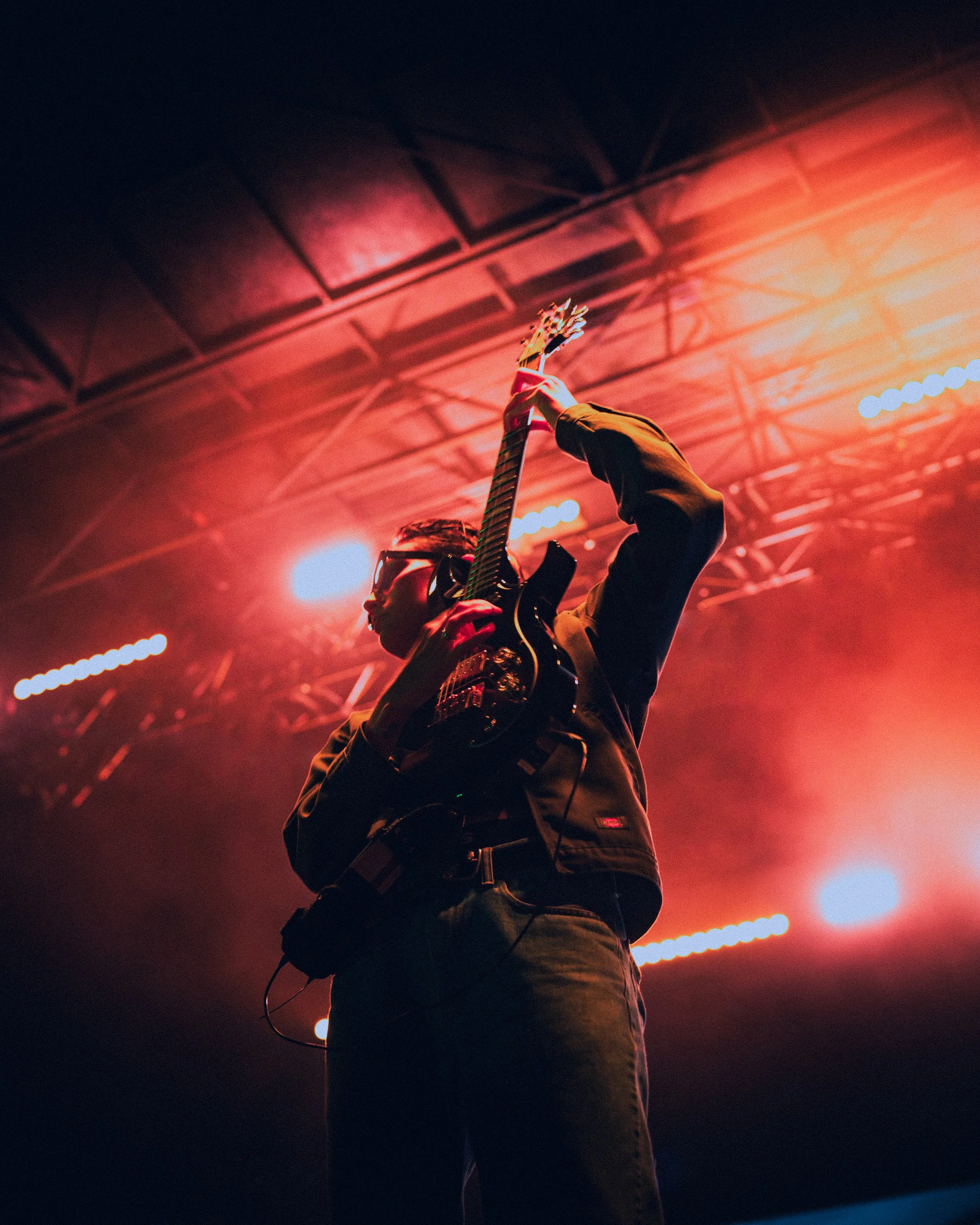 A musician playing an electric guitar on stage under bright red and orange lights.