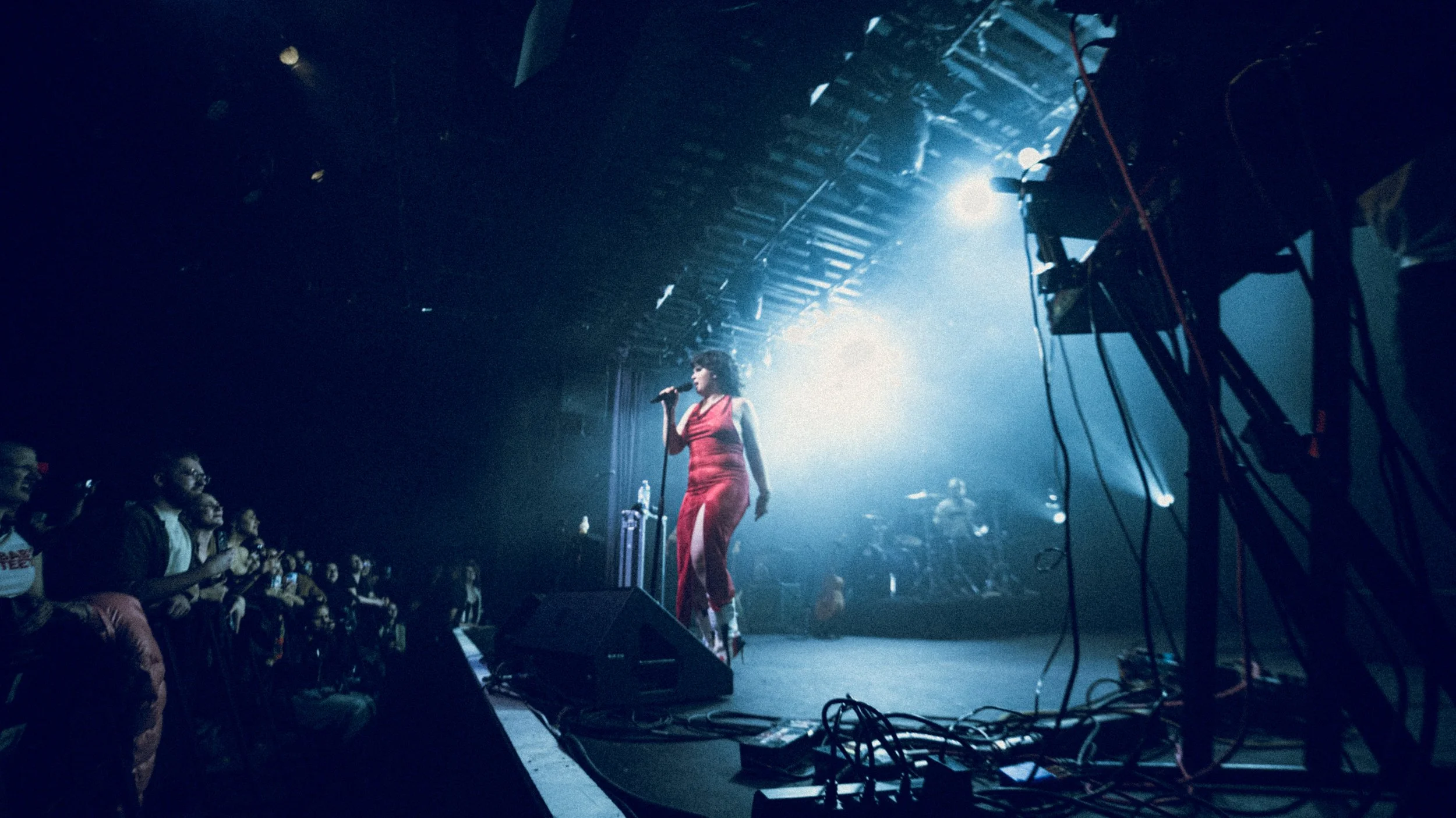 A woman in a red dress singing into a microphone on a stage with band members and audience.