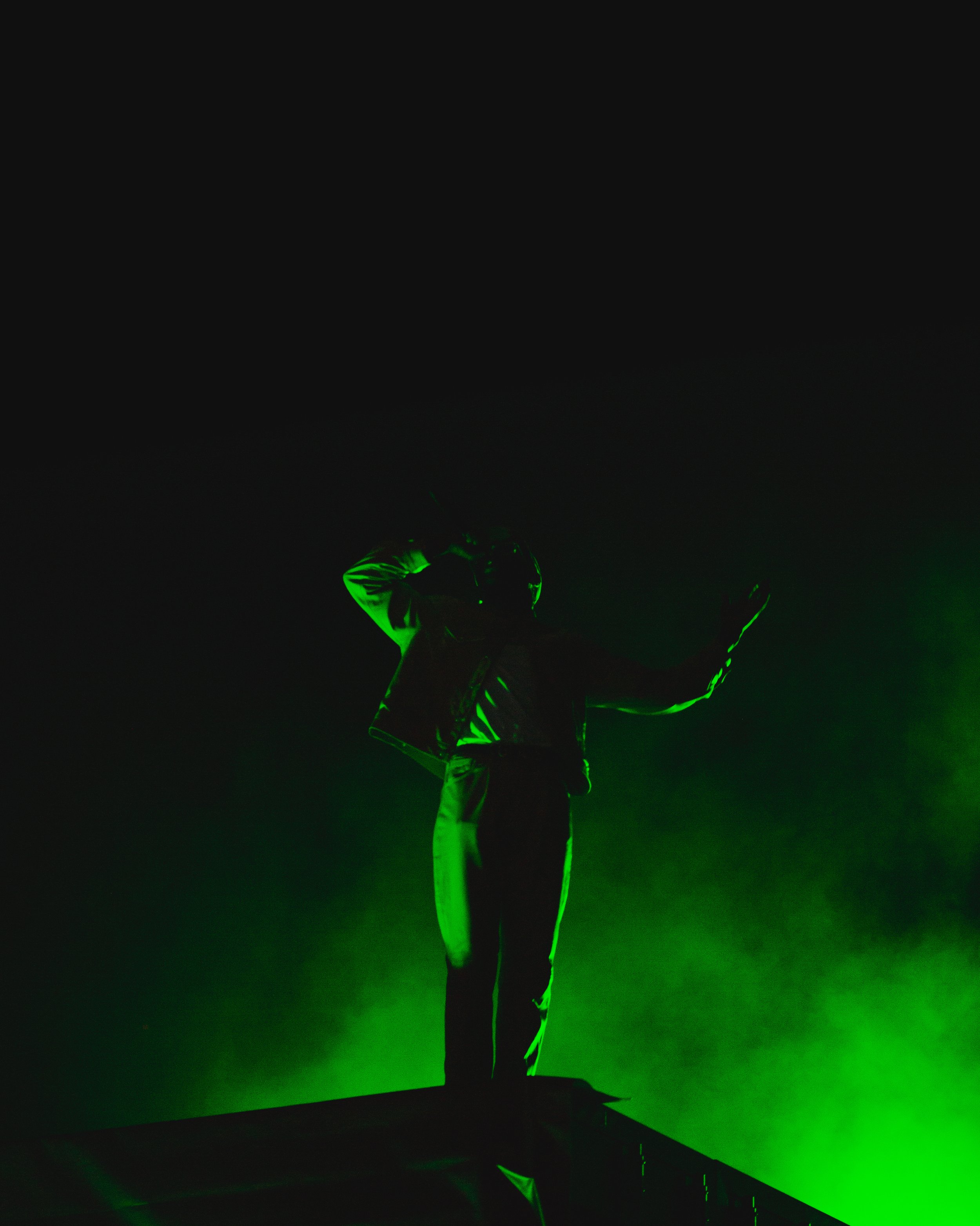 Silhouette of a person standing on a rooftop, illuminated by green light in a dark setting.