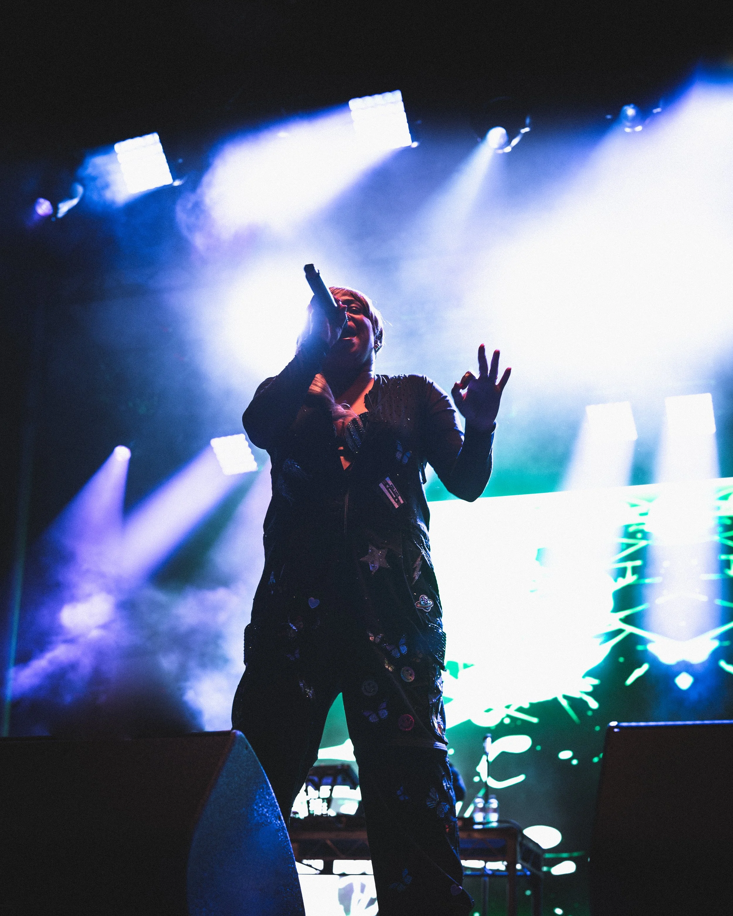 Performer singing on stage with colorful lights and digital background.
