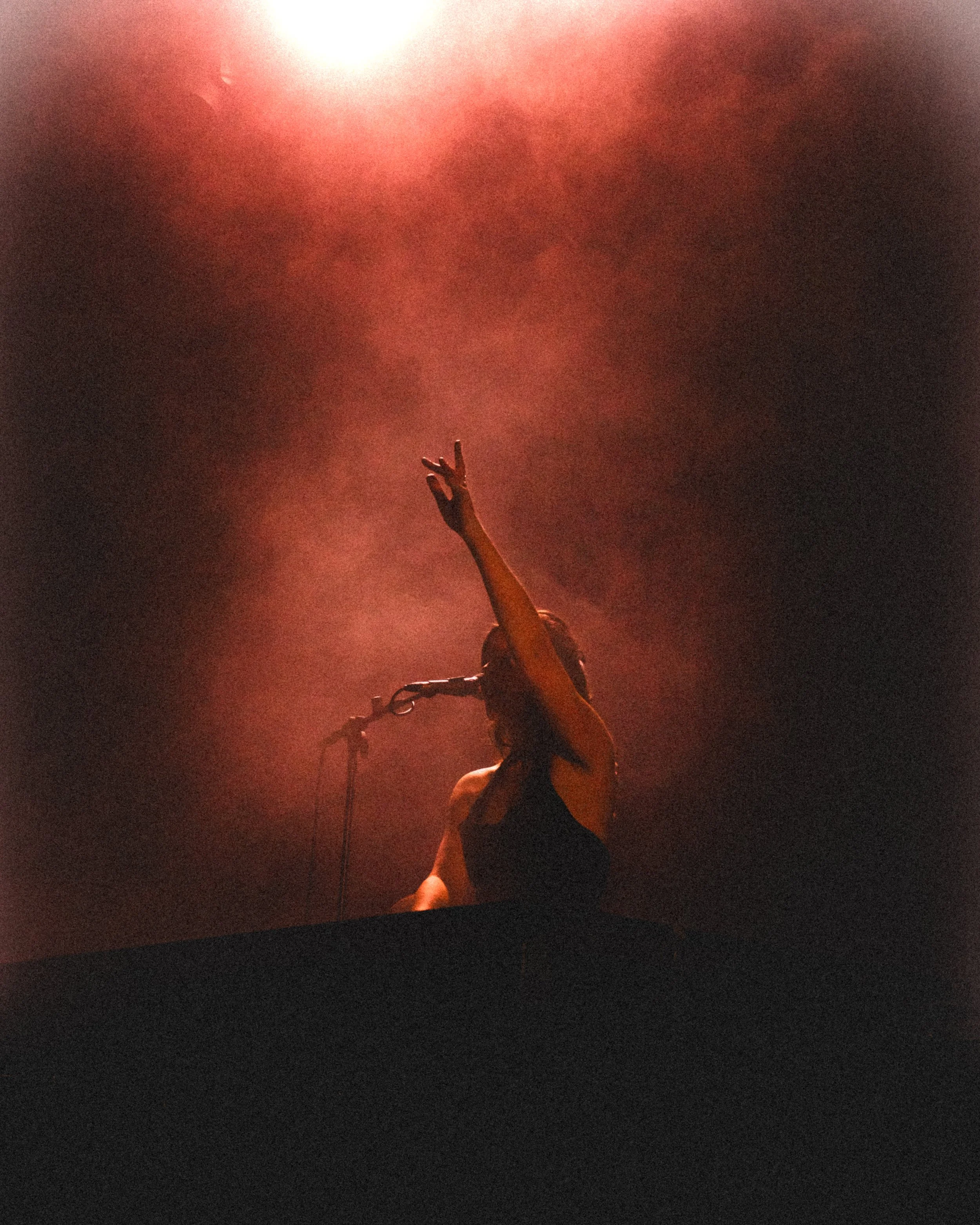 A female singer performing on stage with her arm raised, illuminated by warm stage lights and surrounded by fog.