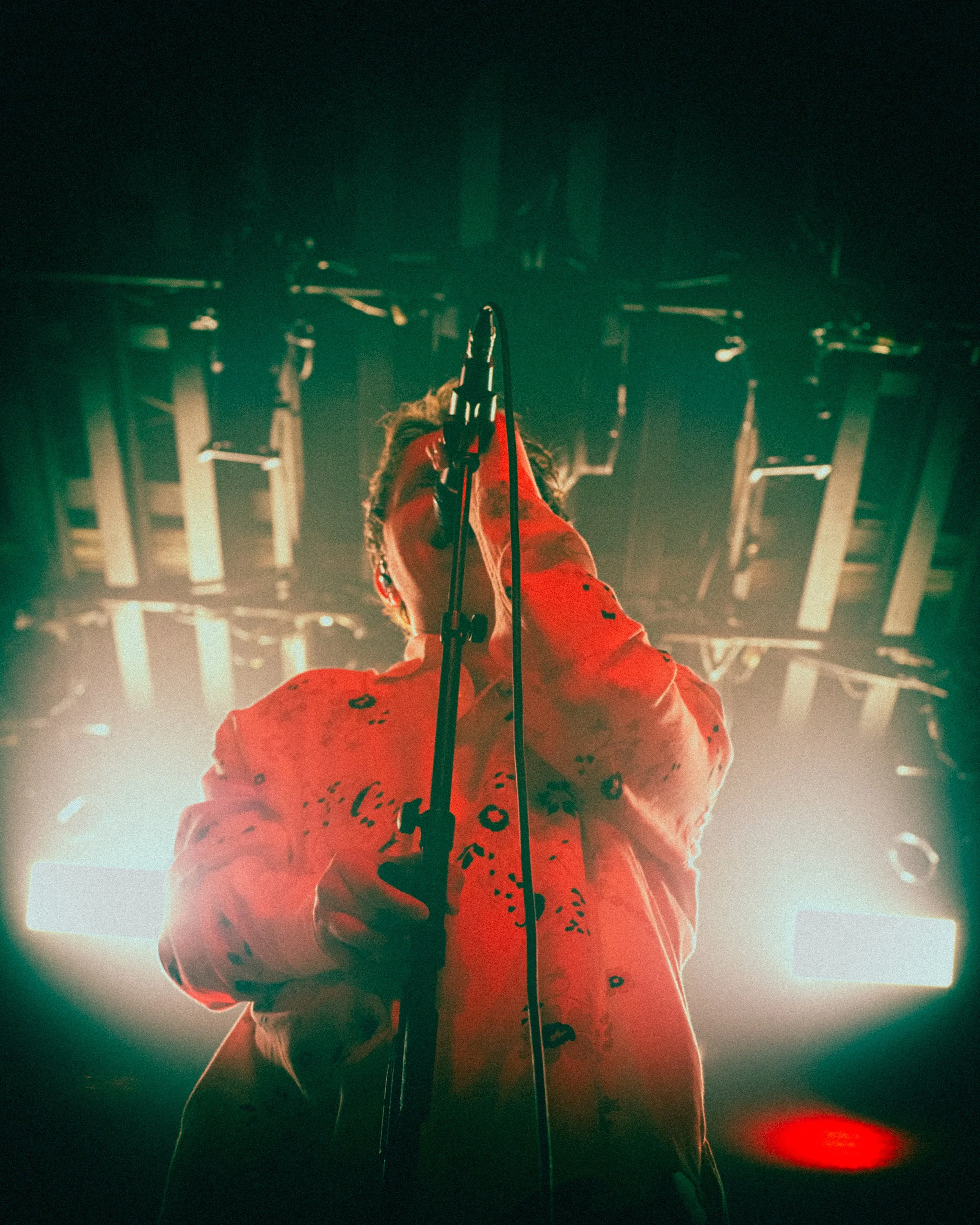 A singer in a red jacket performing on stage under bright lights, holding a microphone.