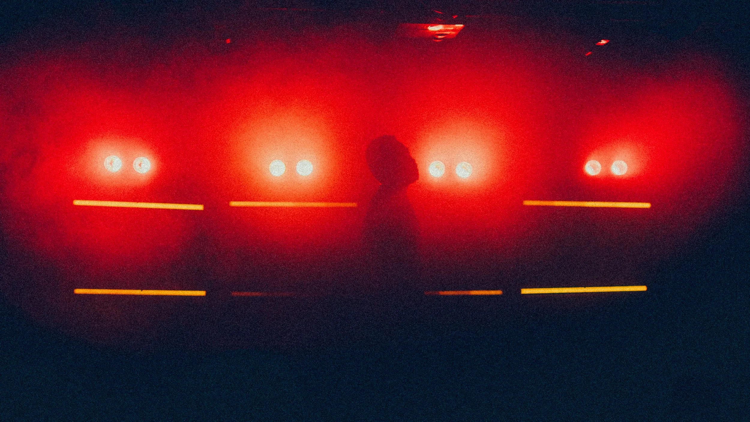 A person standing in front of a wall with glowing red lights and horizontal yellow lines, silhouetted against the bright illumination.