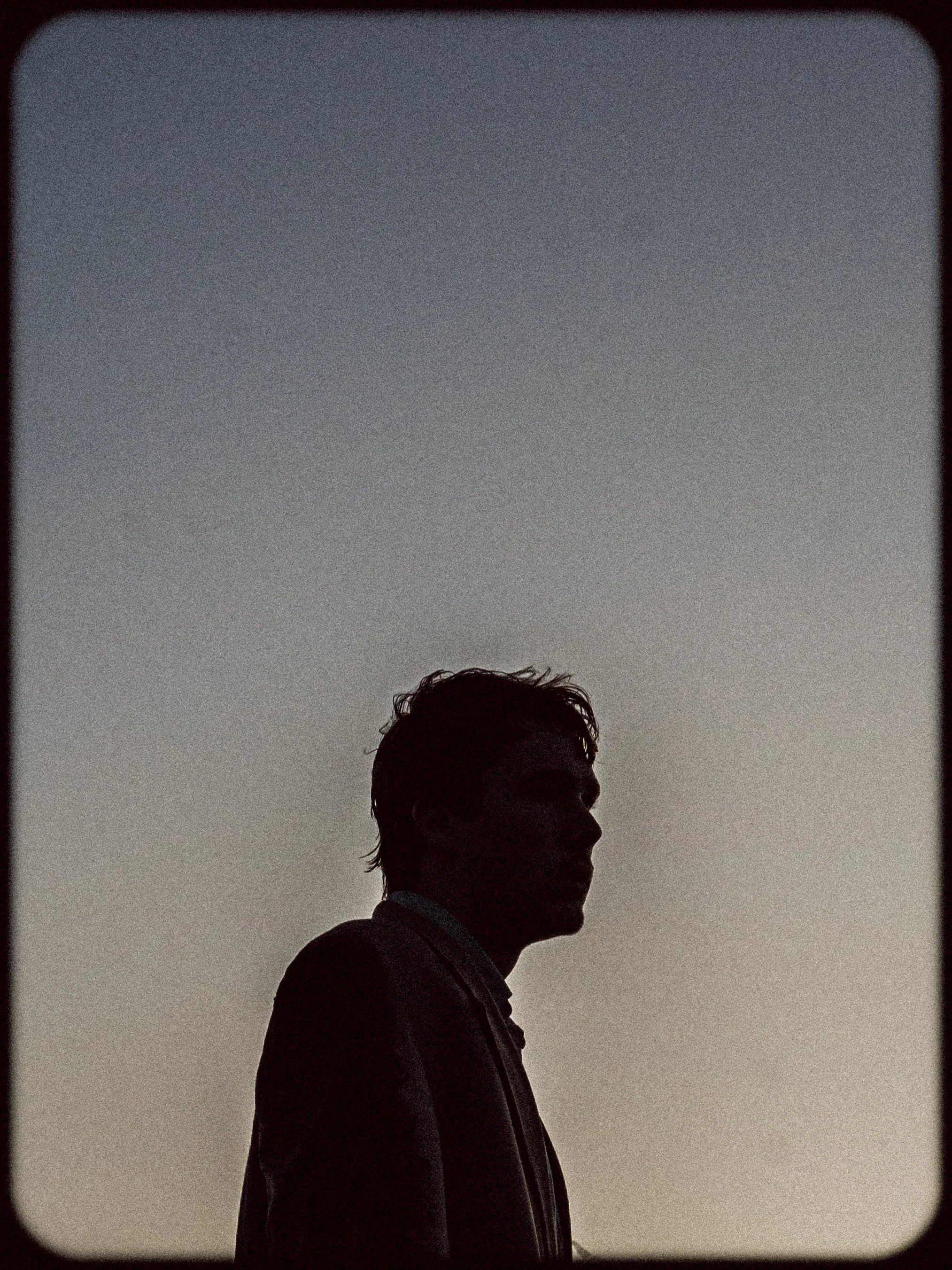 Silhouette of a man in profile against a dusky sky, wearing a jacket.