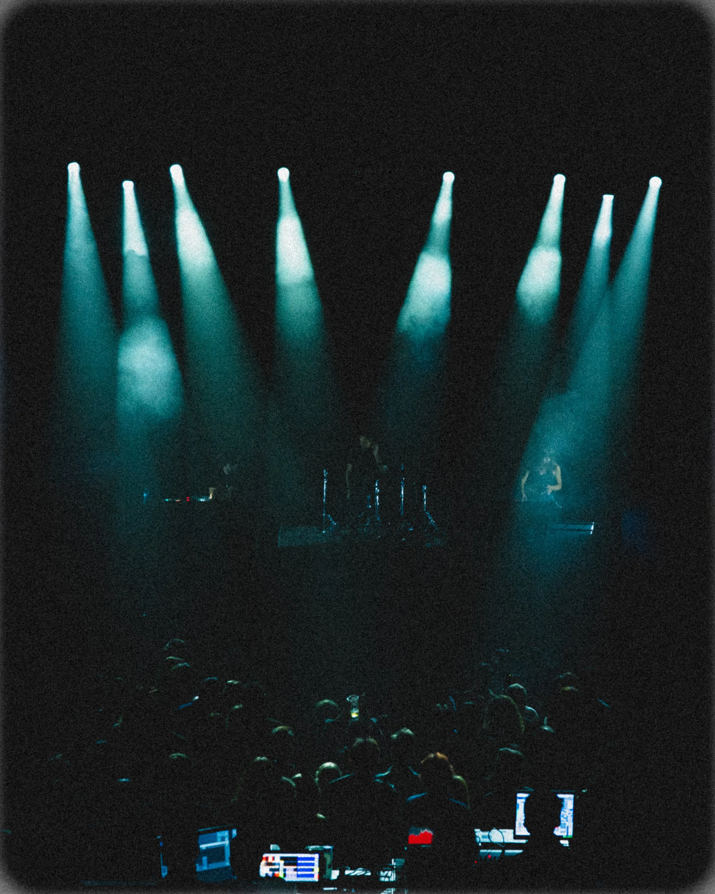 A concert stage illuminated by blue spotlights with musicians performing and an audience in front.