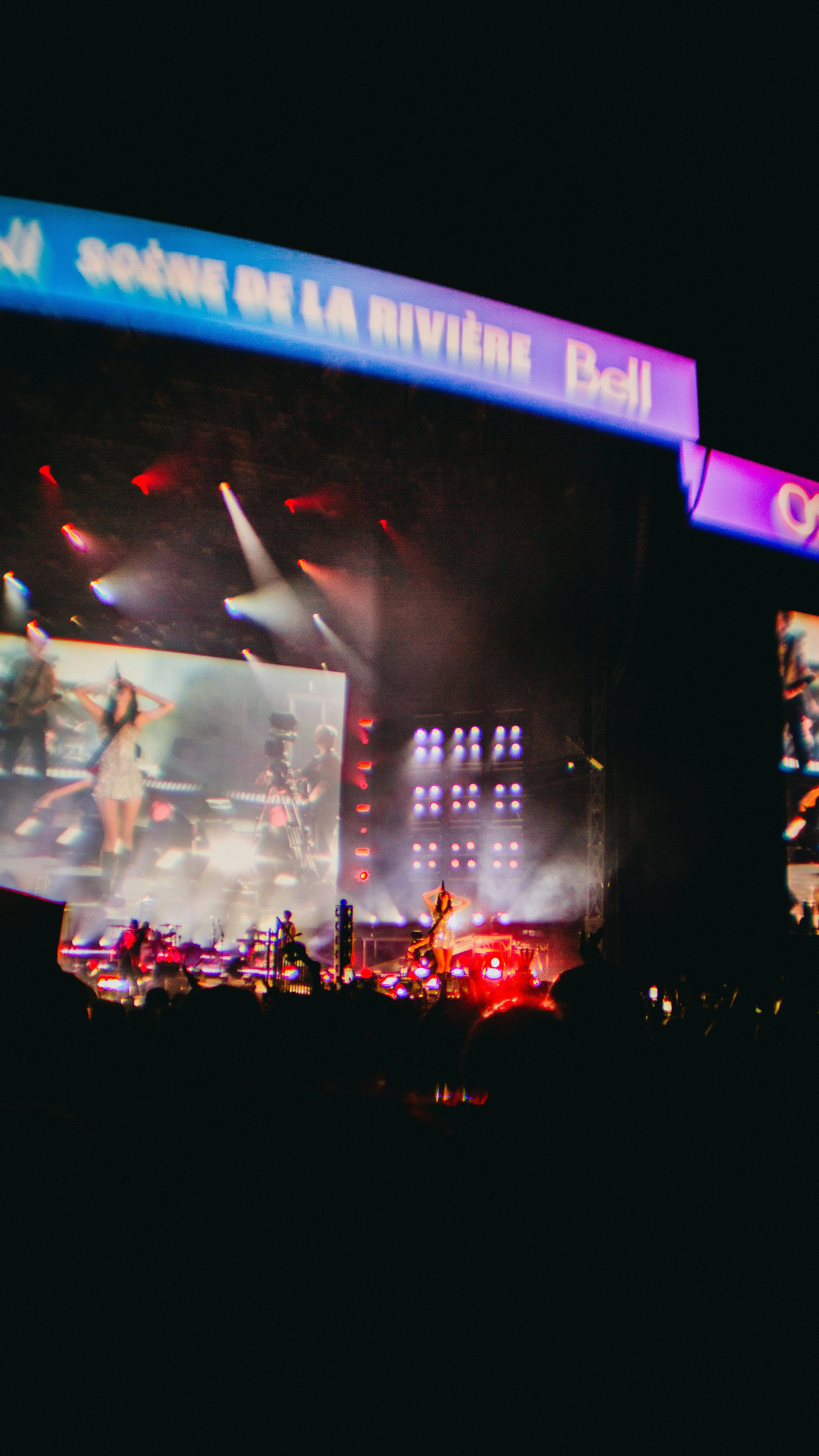 A concert stage at night with performers, stage lights, fog effects, and a large screen showing performers.