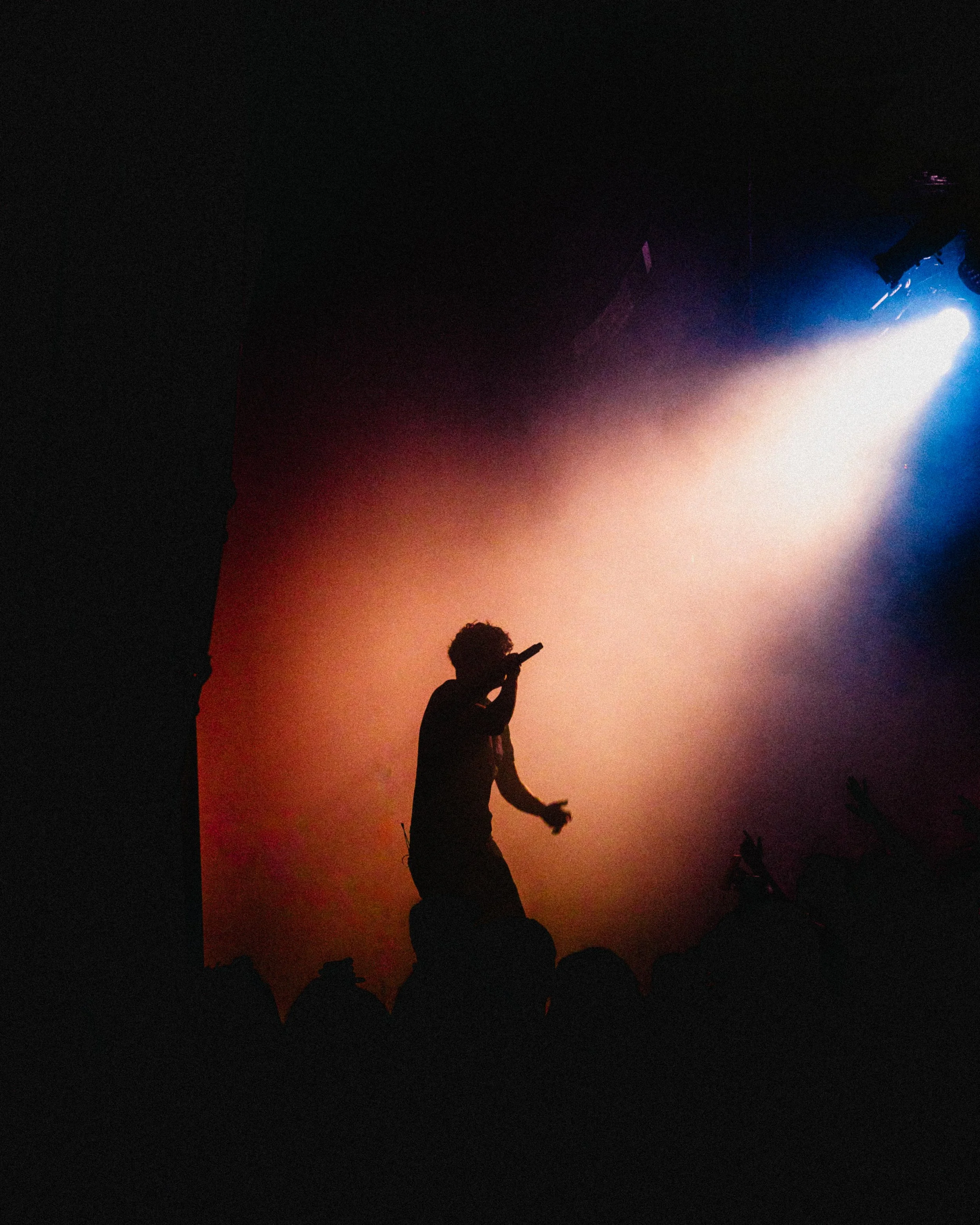 A silhouette of a performer holding a microphone on stage, with colorful stage lights and an audience in front.
