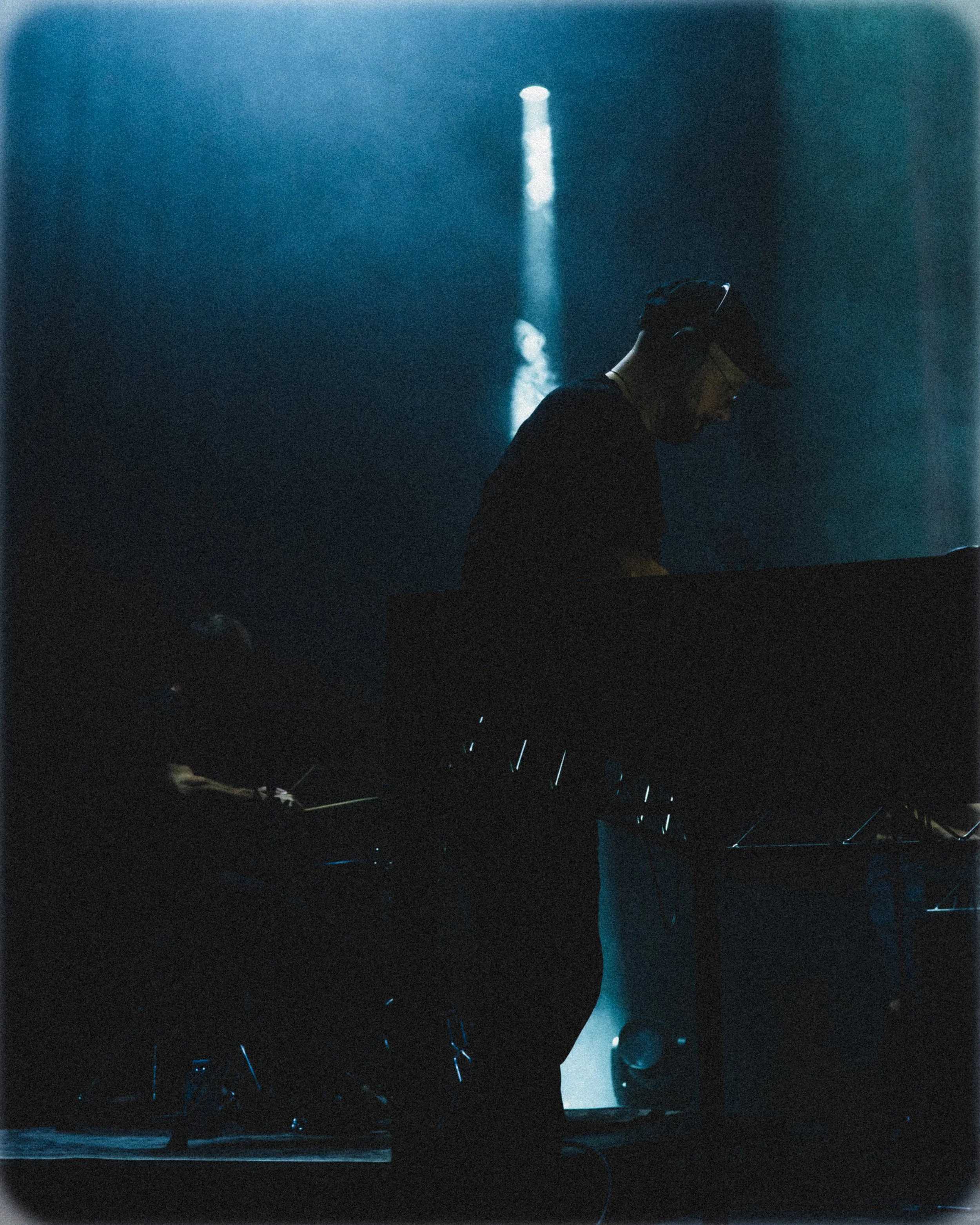 A person wearing a cap and headphones playing a keyboard on stage, with low lighting and a focused atmosphere.