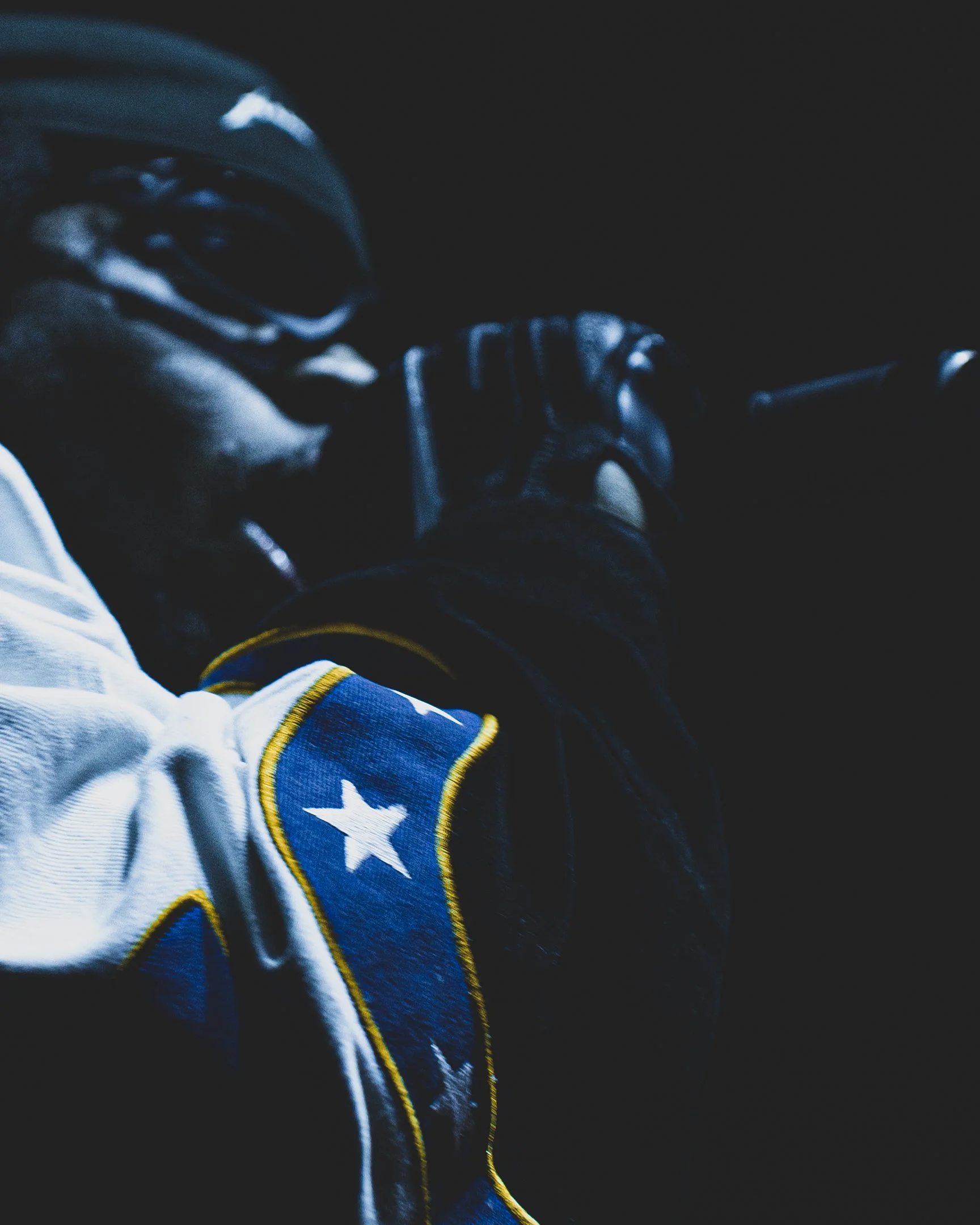 Close-up of a professional ice hockey player wearing a white uniform with a blue and yellow patch, holding a hockey stick, in a dimly lit environment.