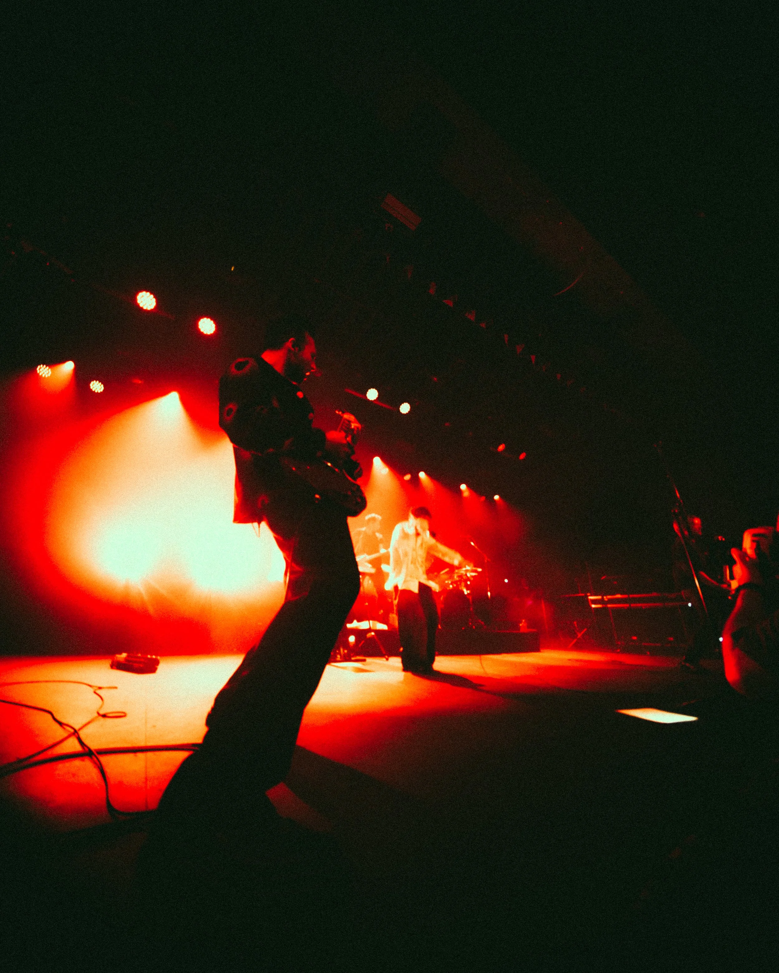 A live music stage with a performer and a photographer capturing the moment, illuminated by red stage lights.