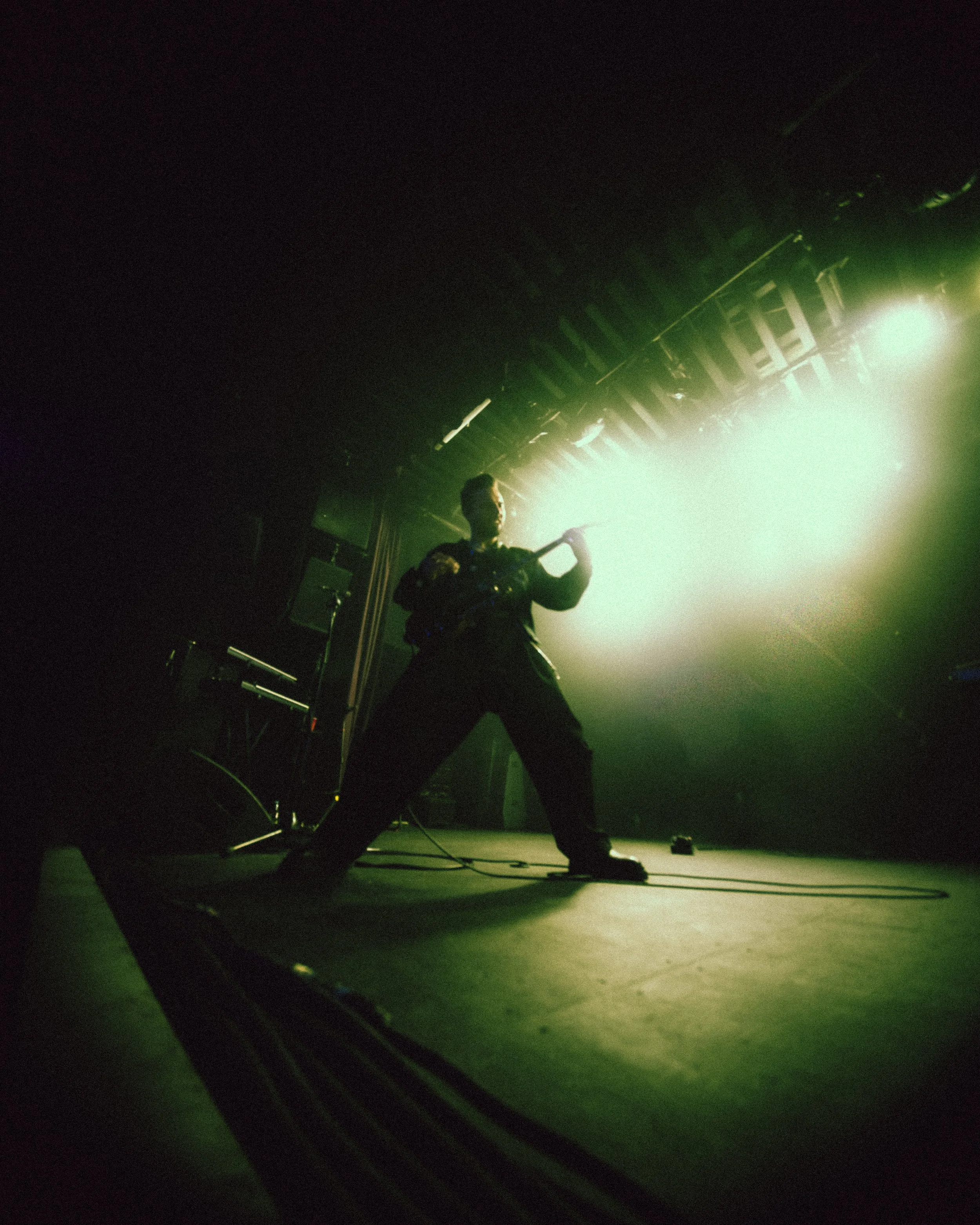 A musician playing an electric guitar on stage with bright green and yellow lighting creating a silhouette effect.