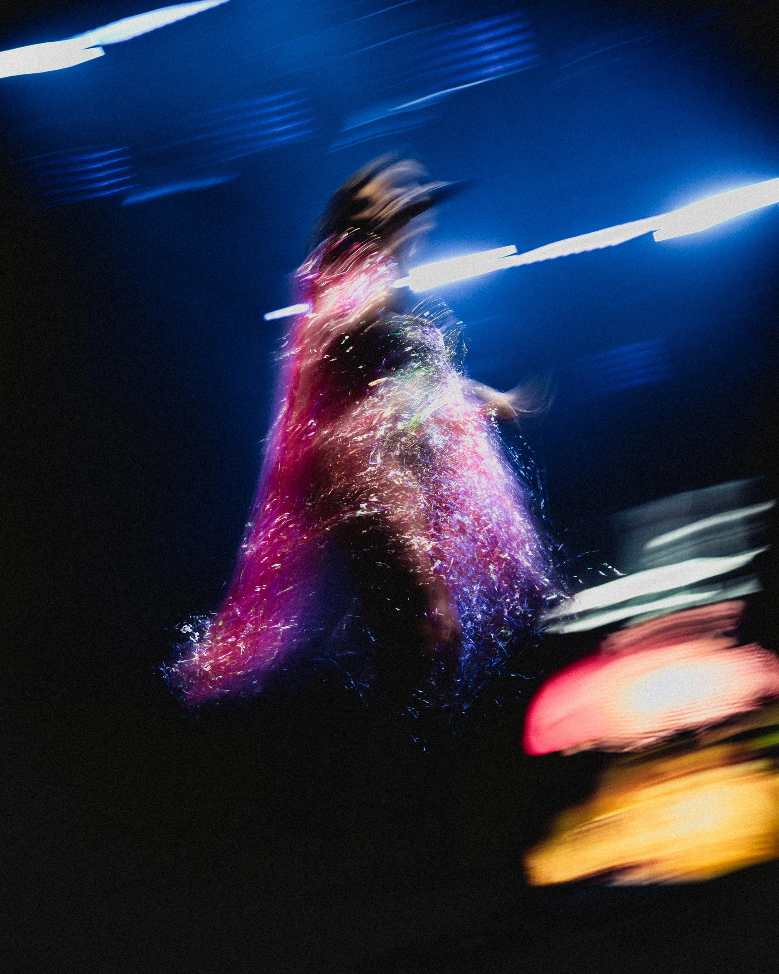 Blurred image of a woman in a dark setting, illuminated by colorful lights, with motion effect