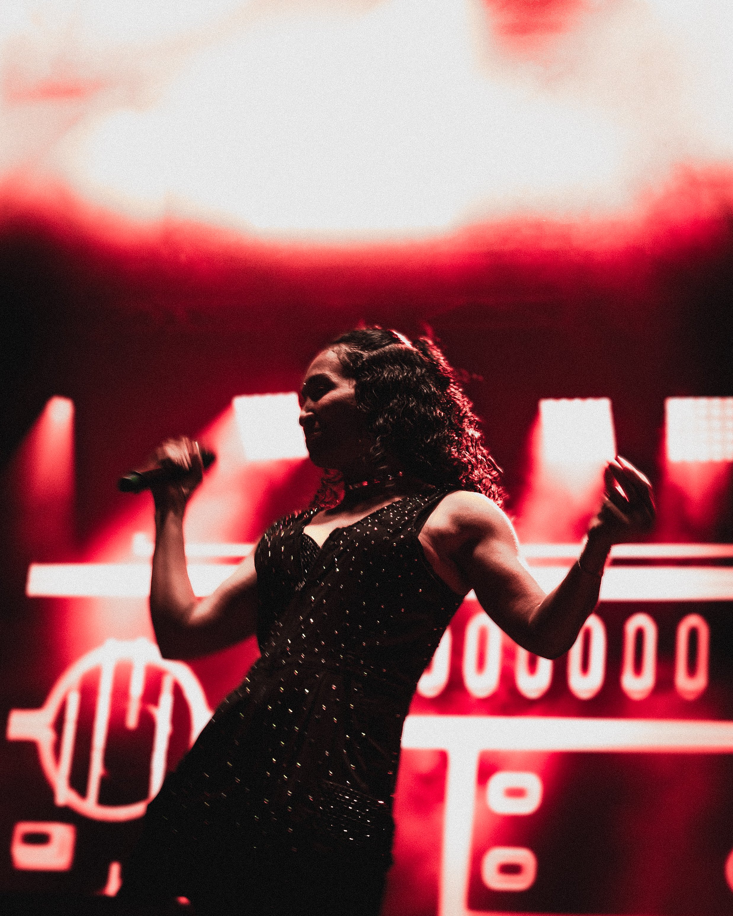 A woman singing on stage with red lighting and a large screen in the background.