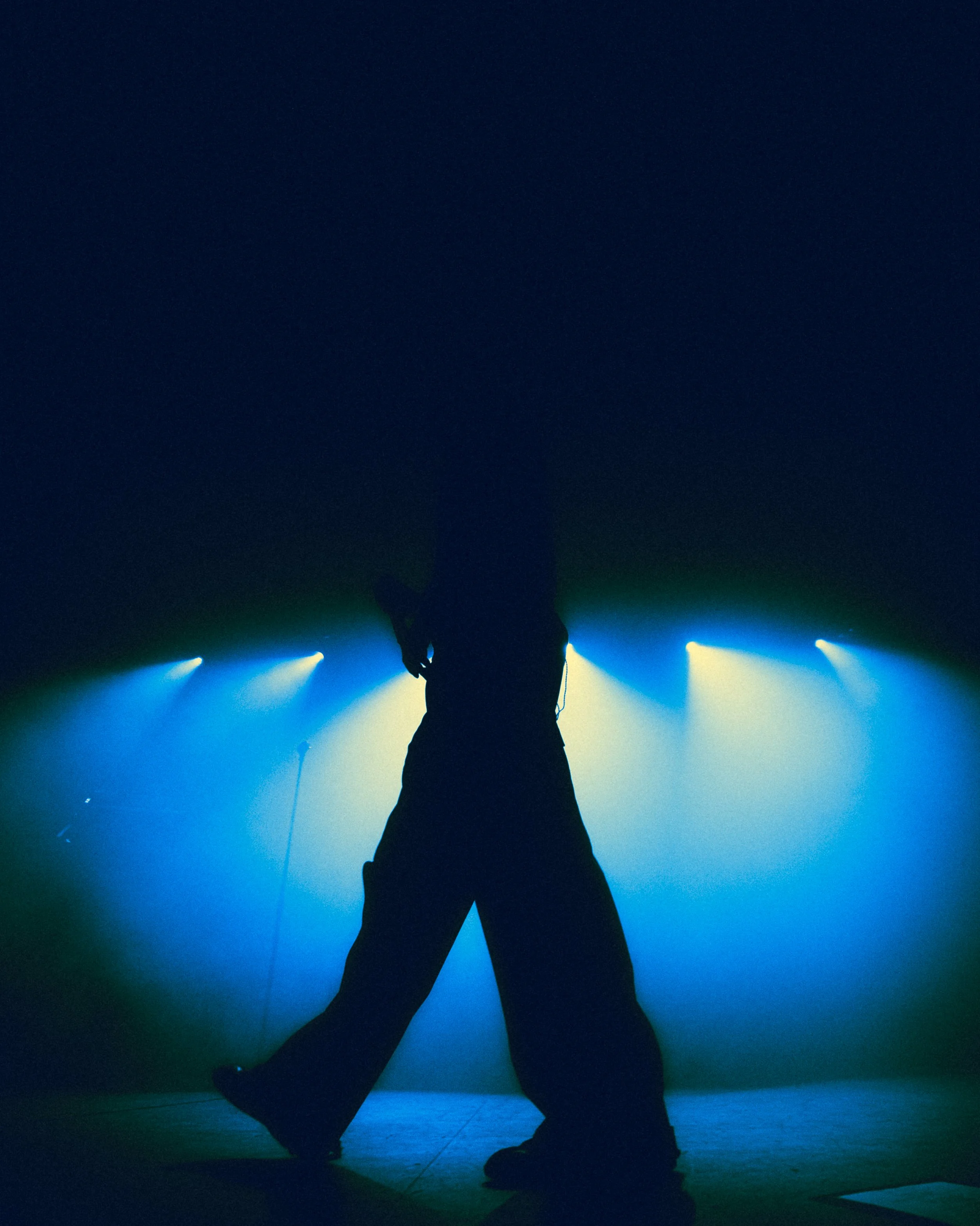 Silhouette of a person standing on a stage with blue and yellow spotlights behind them.