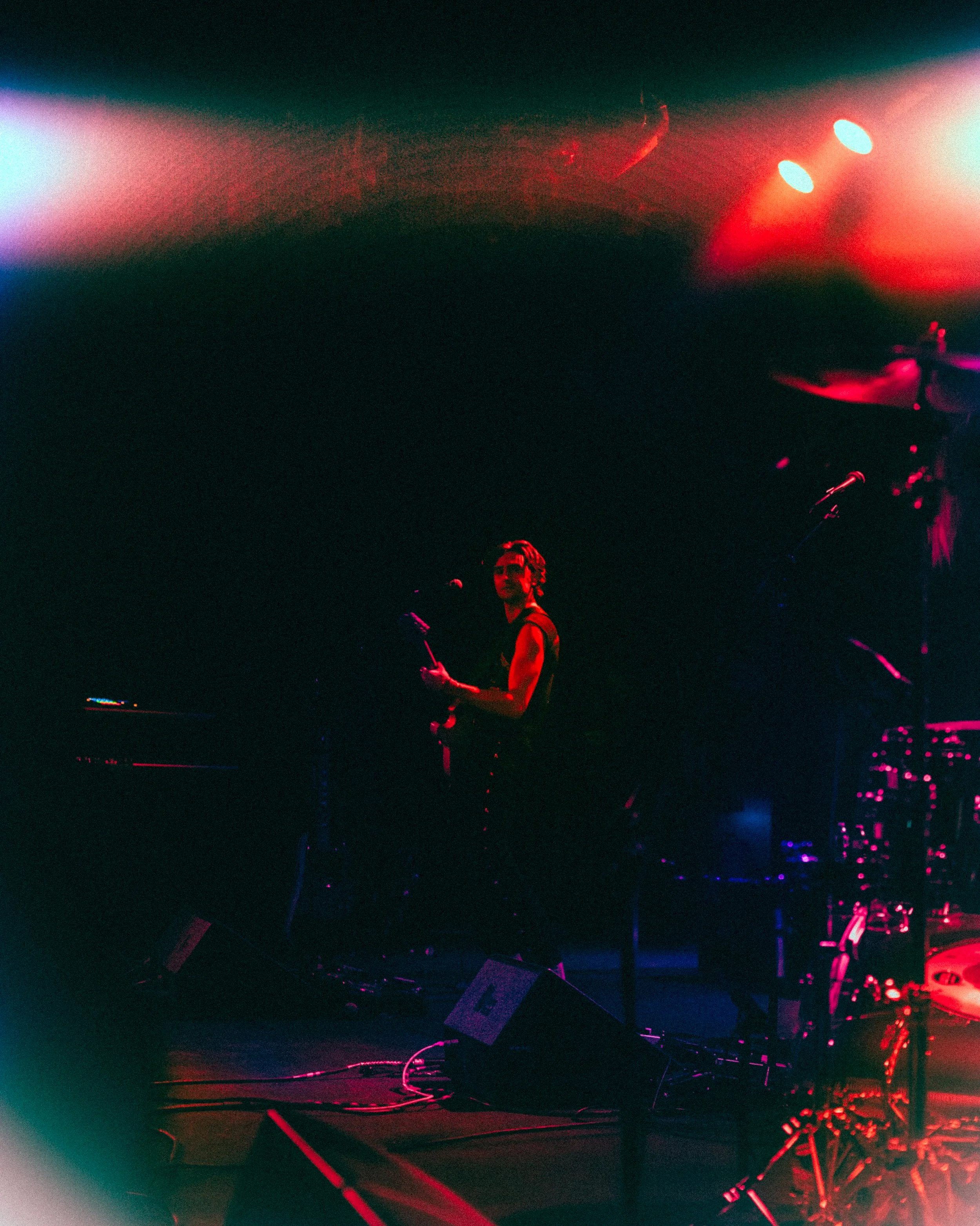 A musician performing on stage under colorful lights, playing guitar and singing into a microphone with a dark background.
