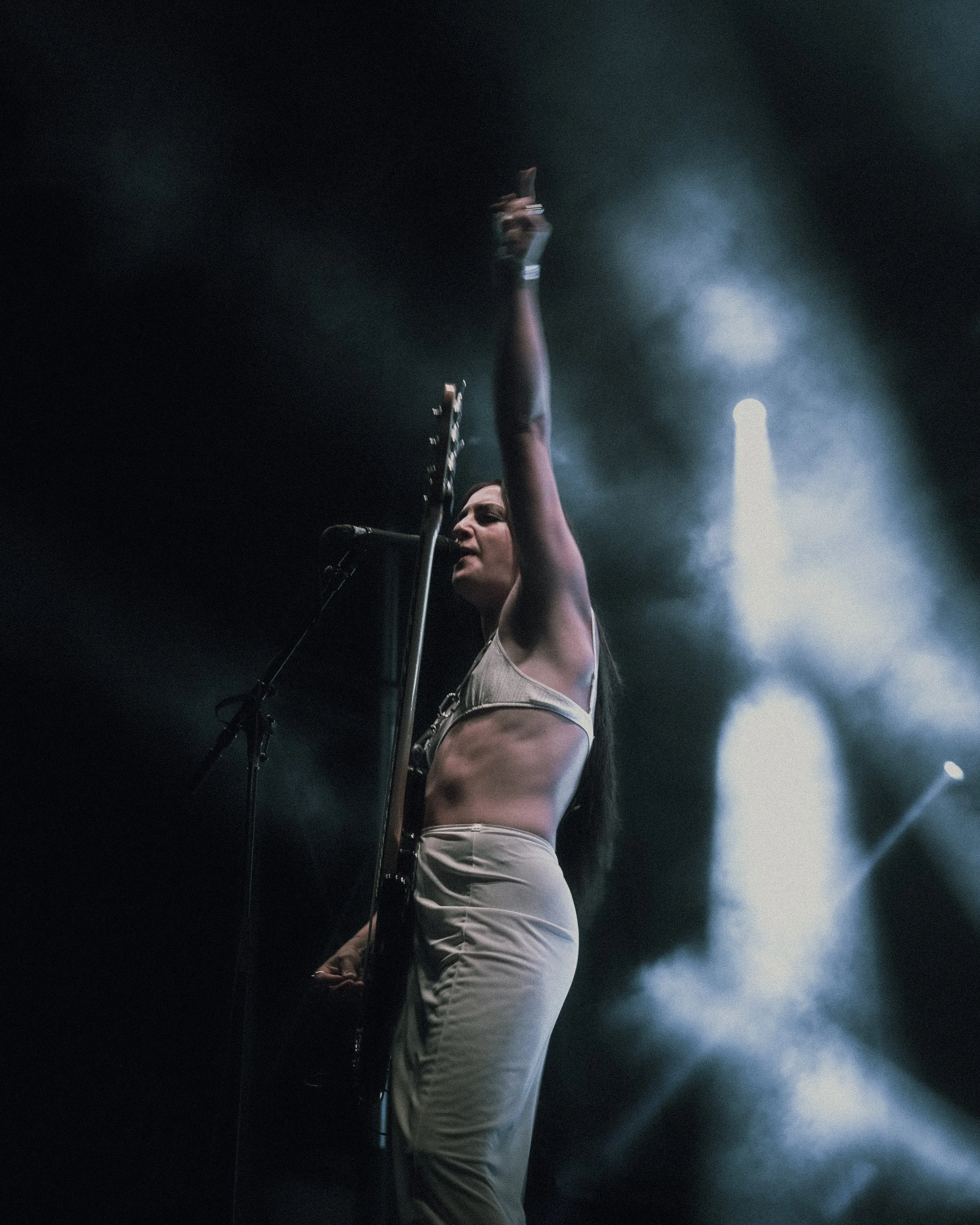 Female musician playing guitar and singing on stage with spotlight and smoke effects.