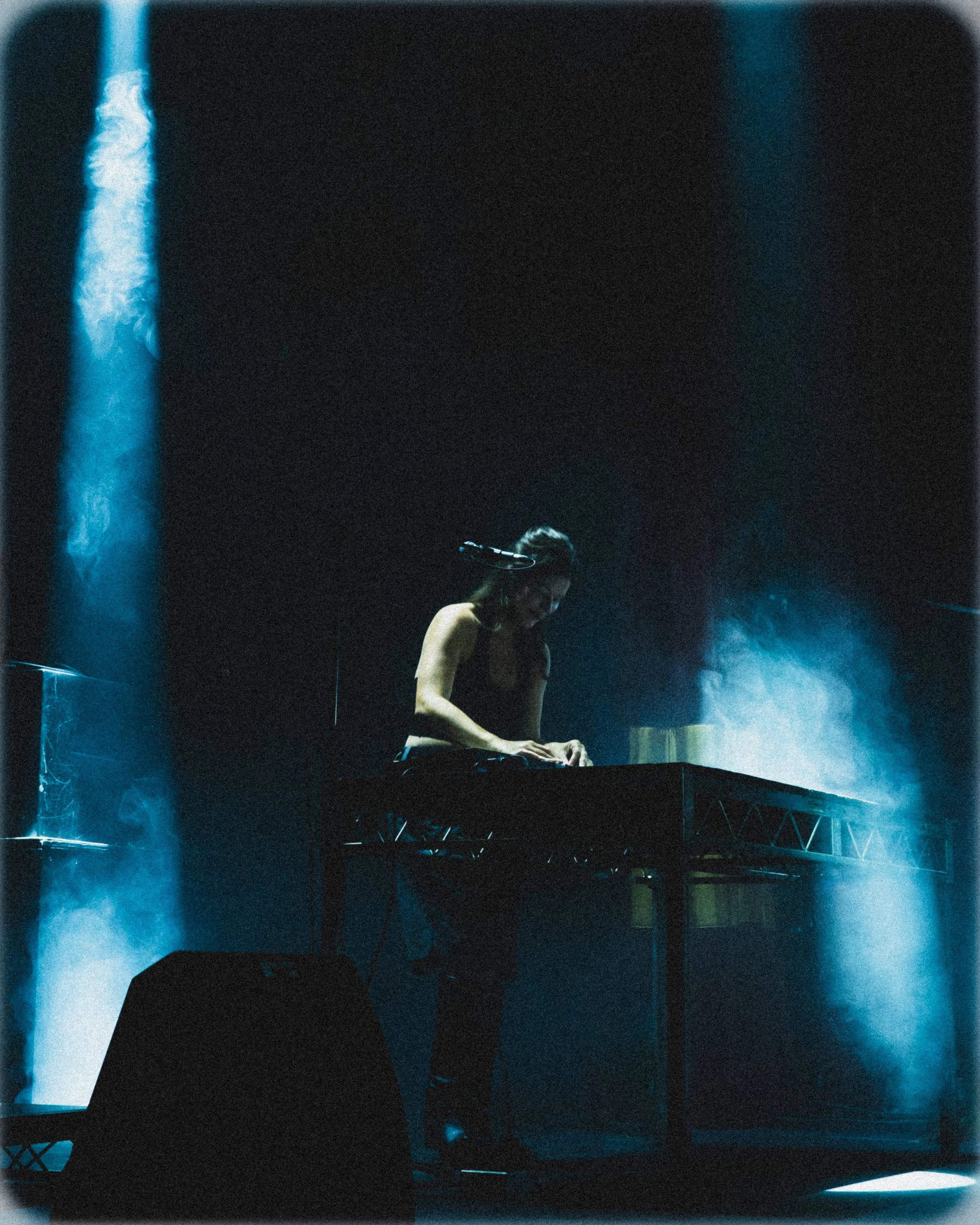 A woman performing on stage with a keyboard, surrounded by blue stage lights and smoke.