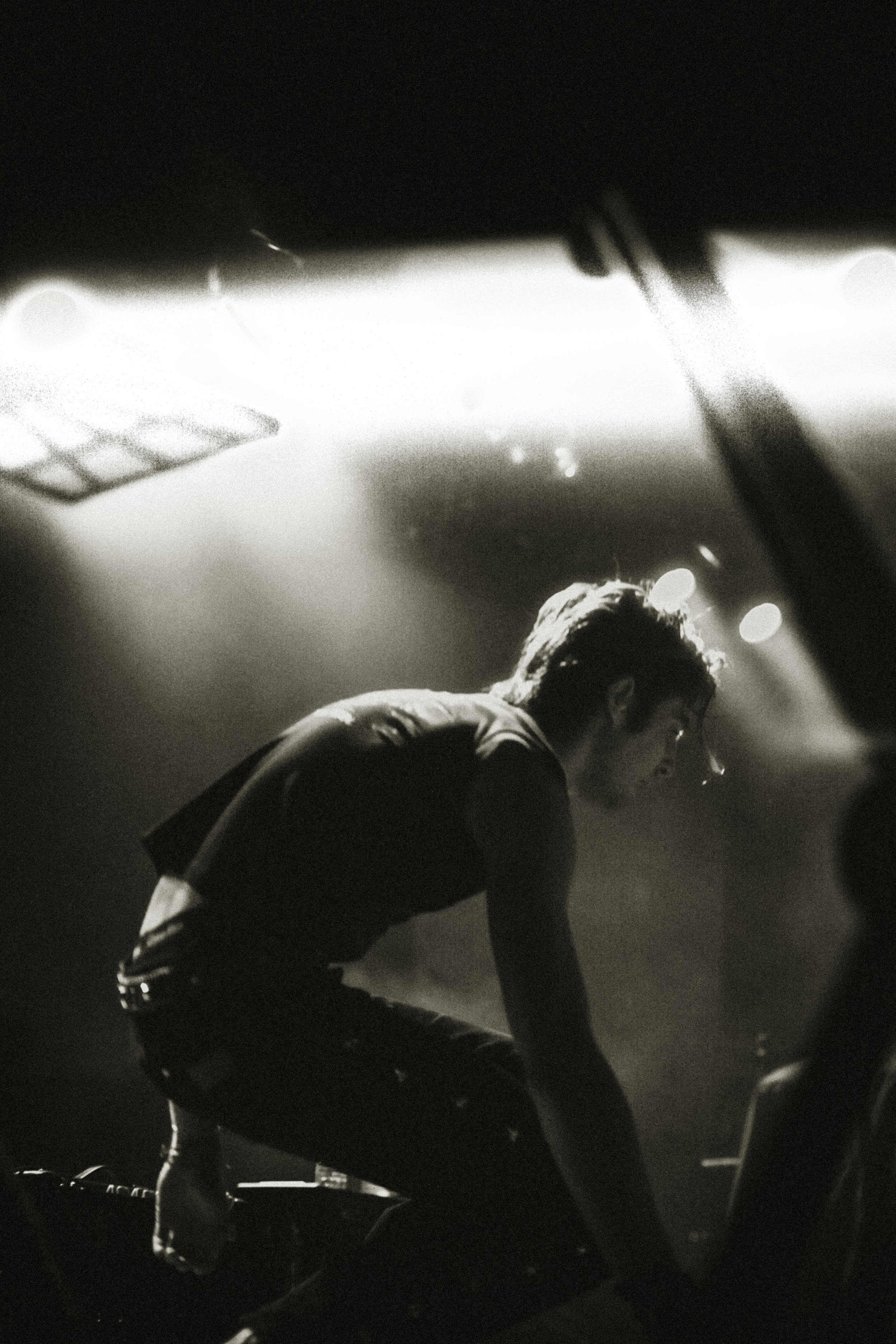 A person seen through a car's windshield, leaning forward, with stage or concert lighting in the background.