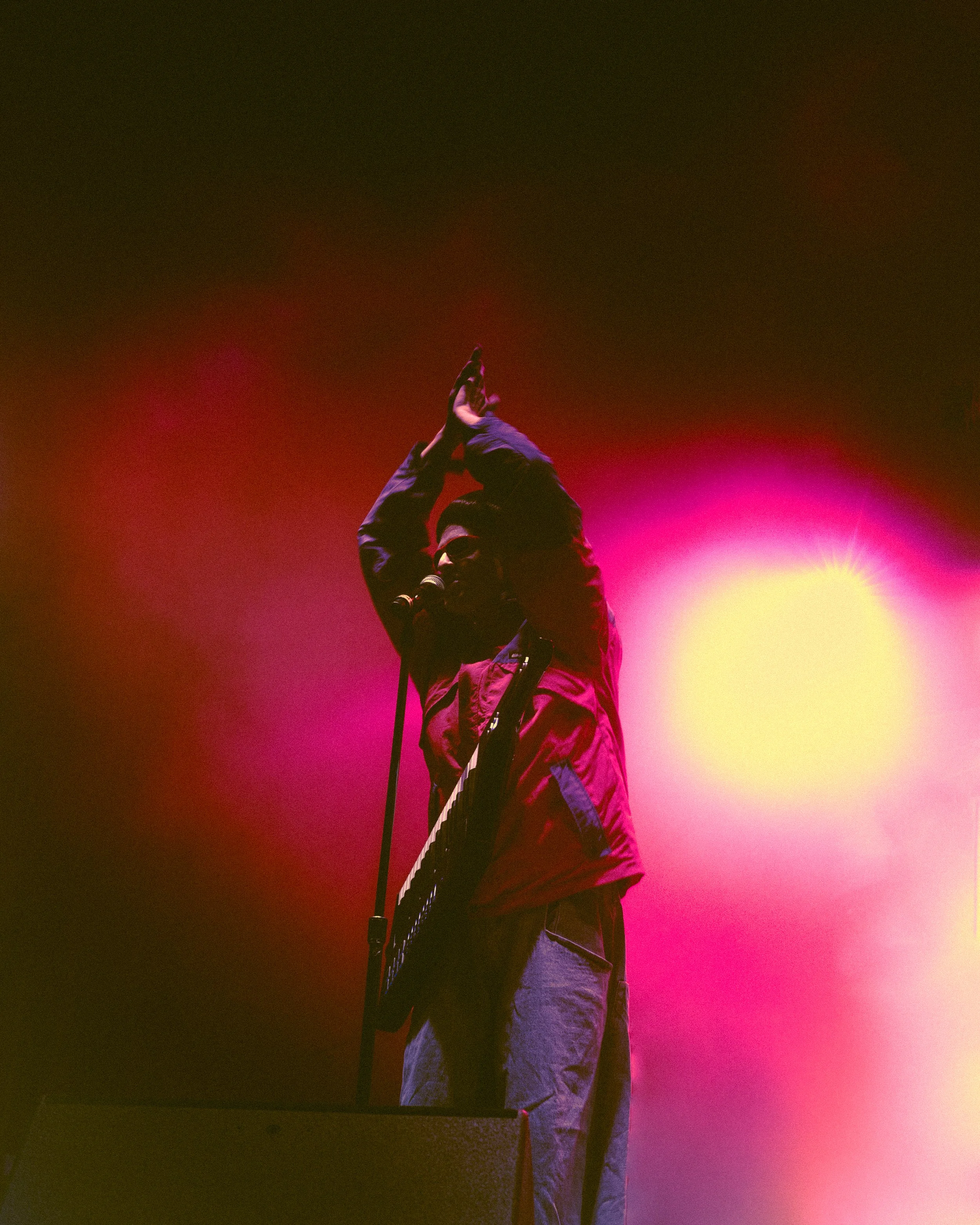 A person performing on stage with colorful pink and yellow stage lights.