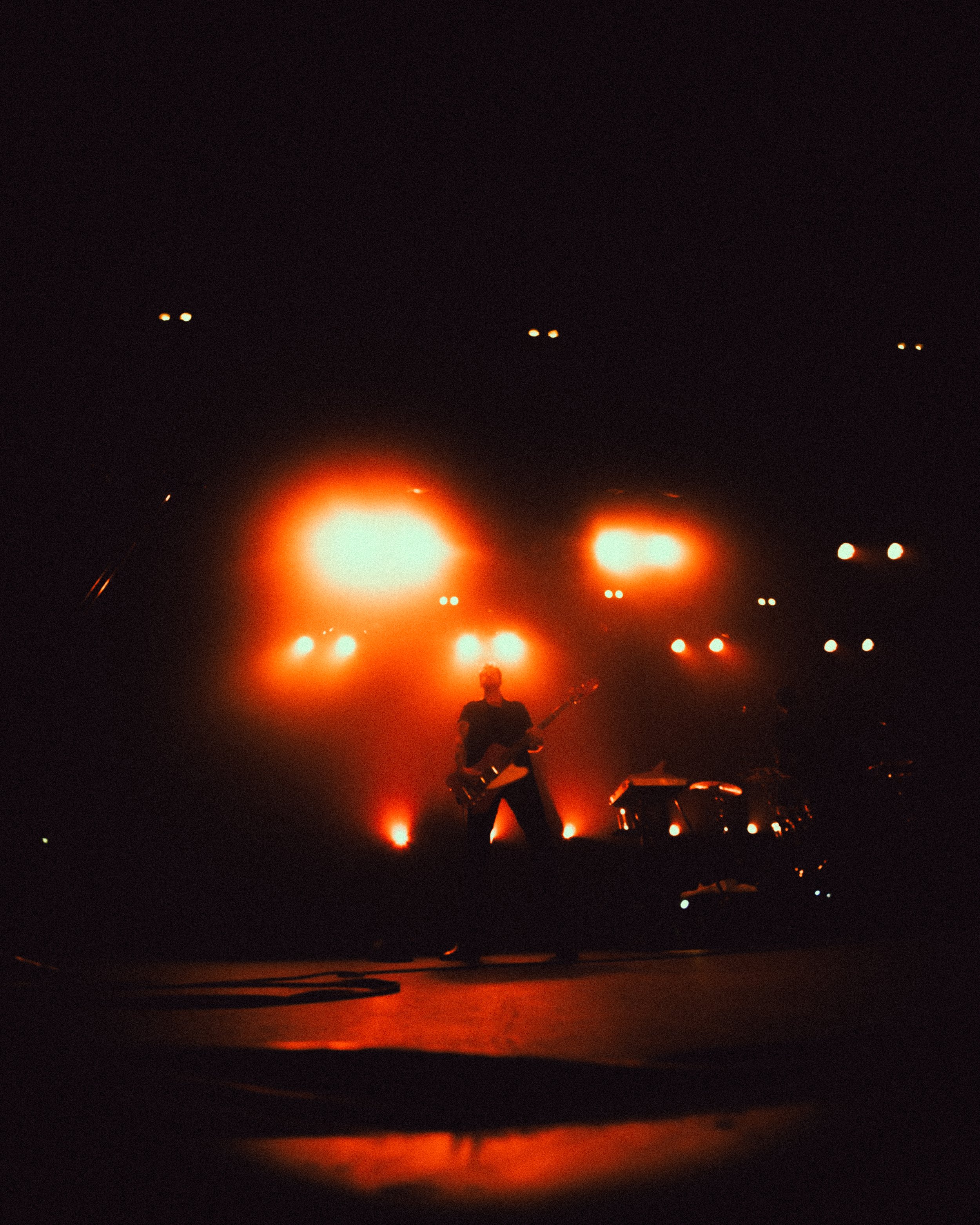 A musician playing a guitar on stage during a concert with orange and red stage lights.