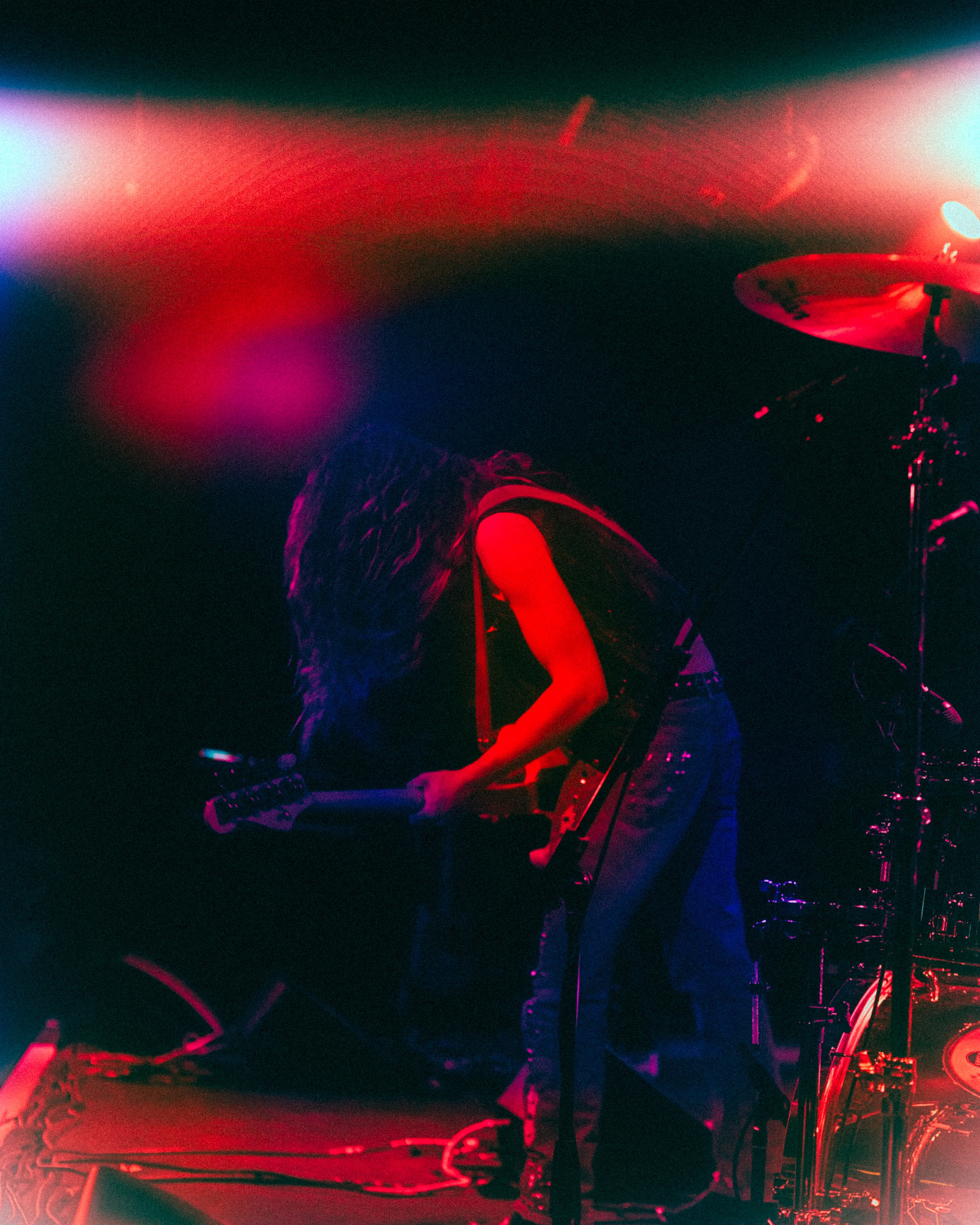 A person with long hair playing an electric guitar on stage with red and blue lights.