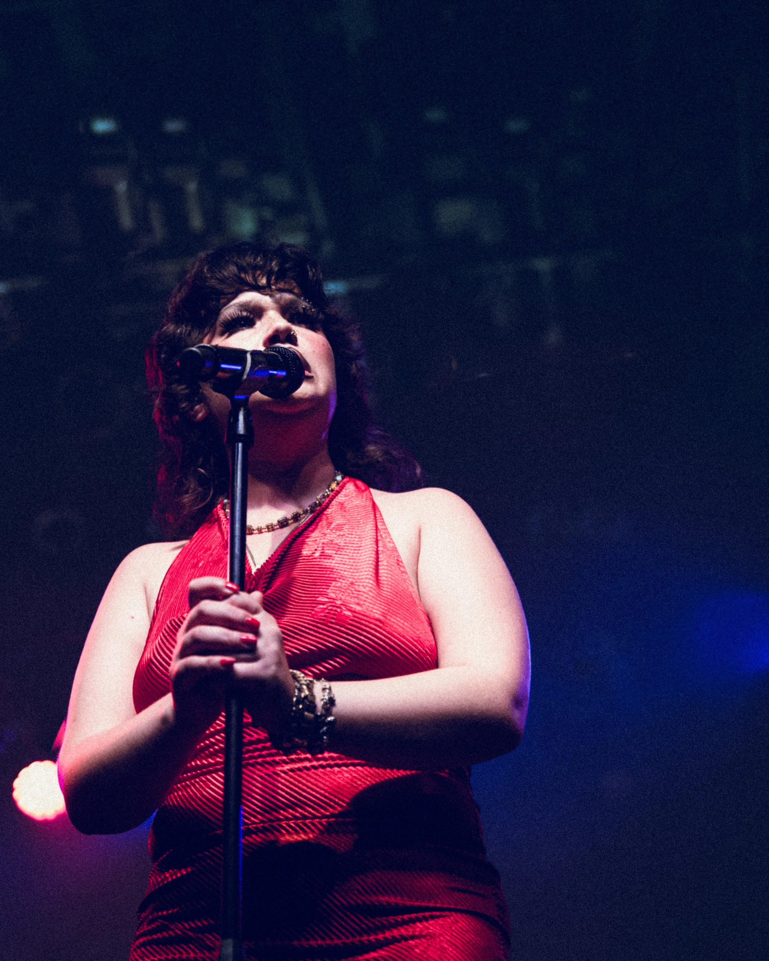 A woman singing into a microphone on stage, wearing a red dress.