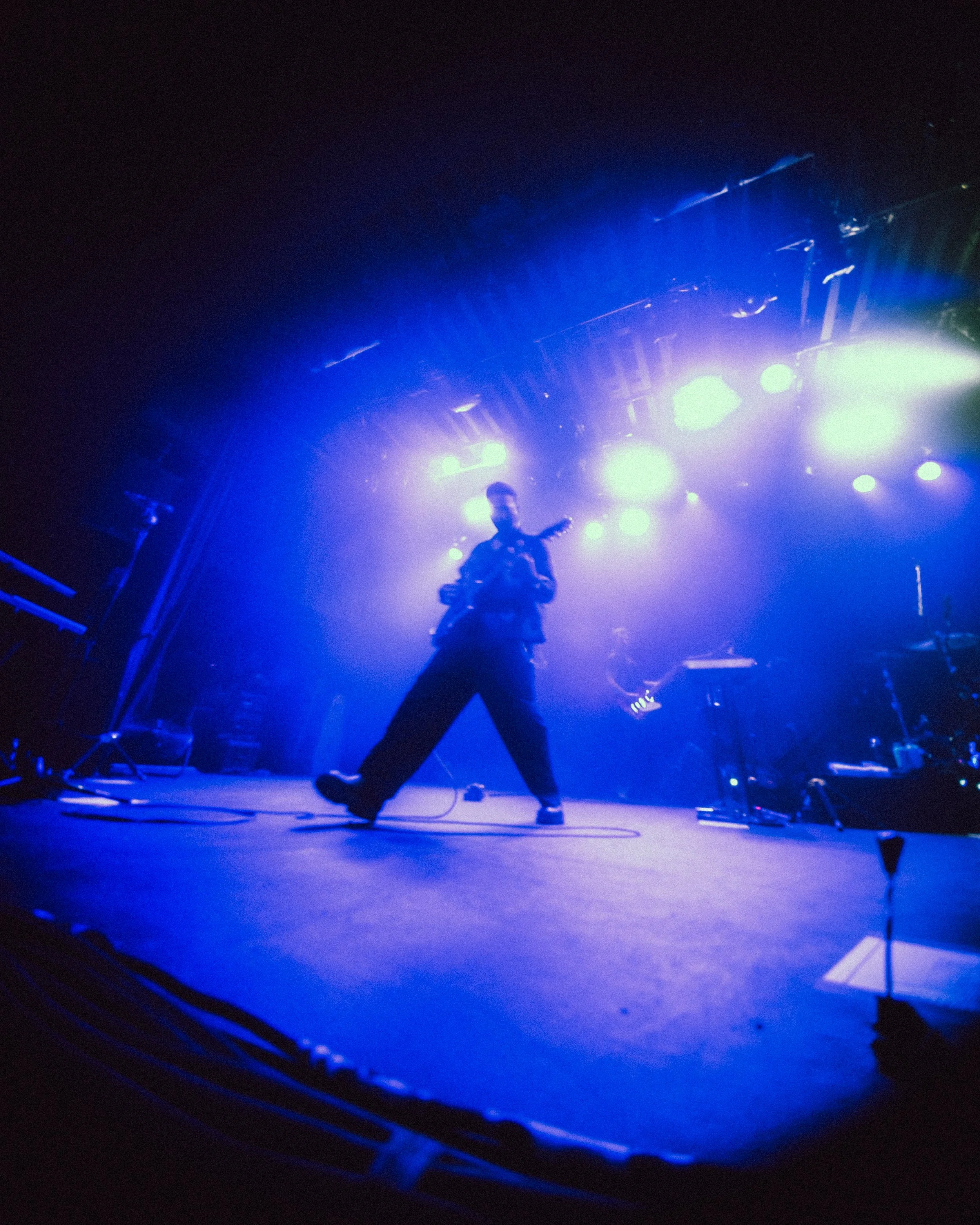A musician playing guitar on stage with intense blue and purple lighting.