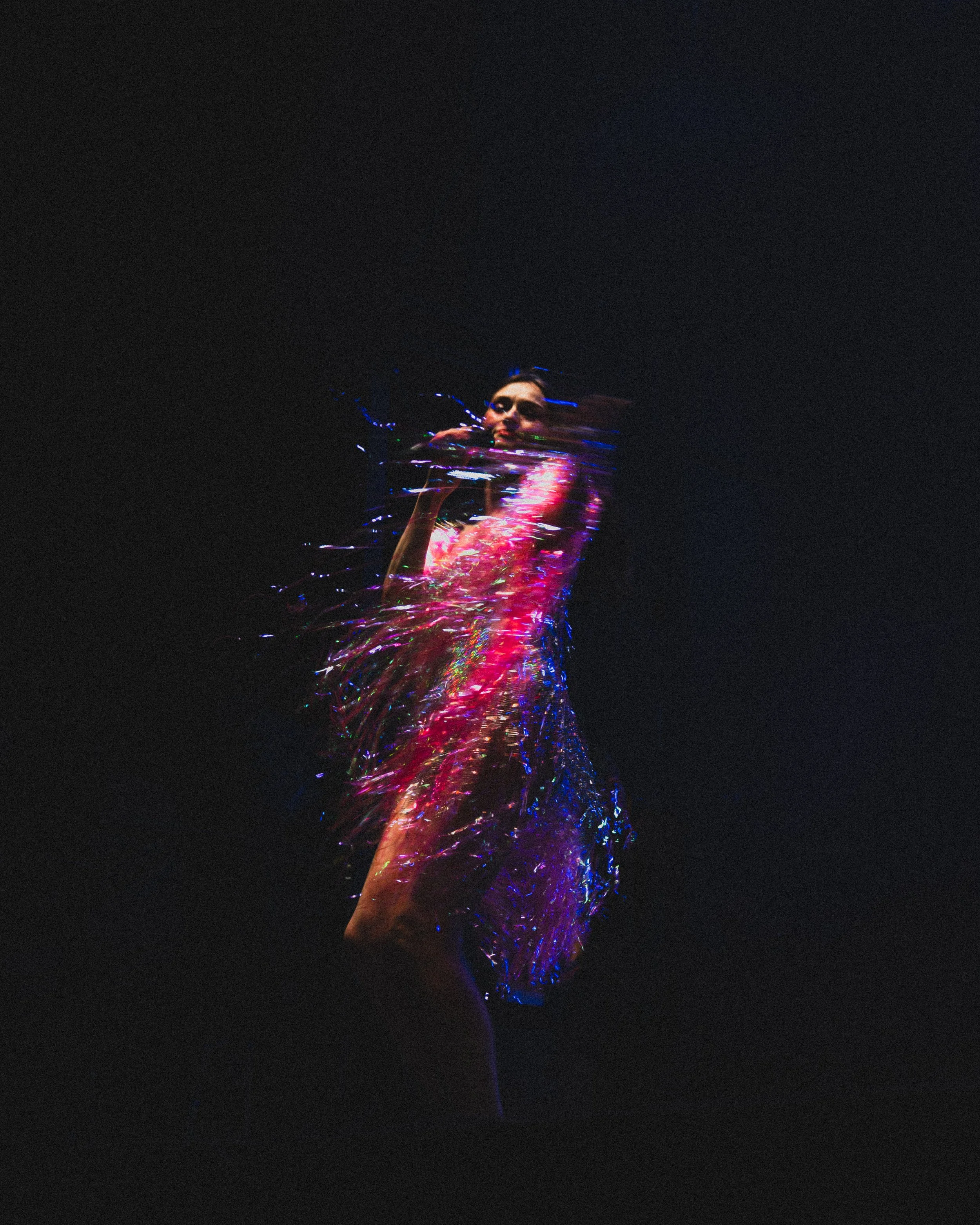 A woman dancing in a black dress with colorful, glowing light effects against a dark background.