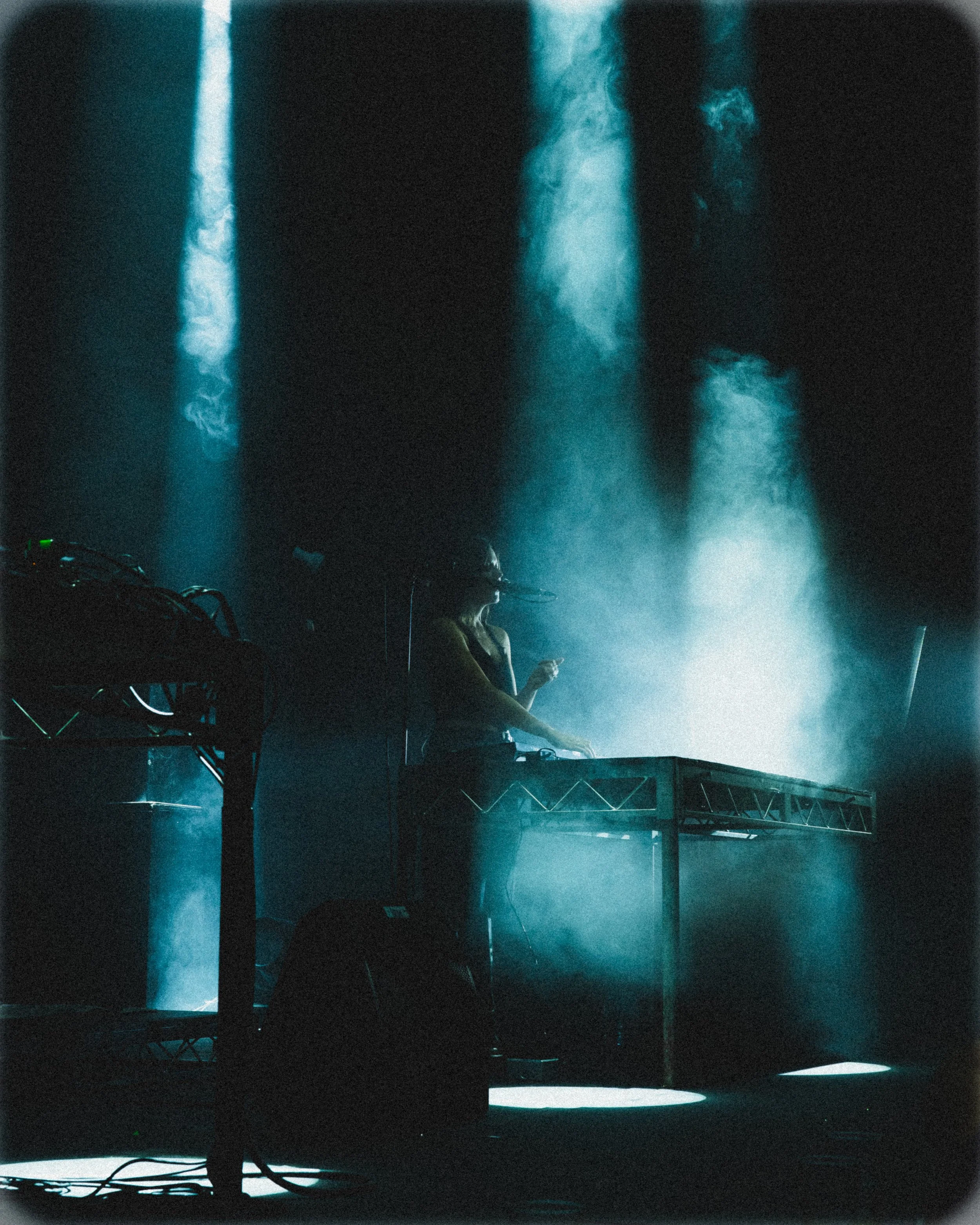 A DJ performing on stage with smoke and blue lighting effects.