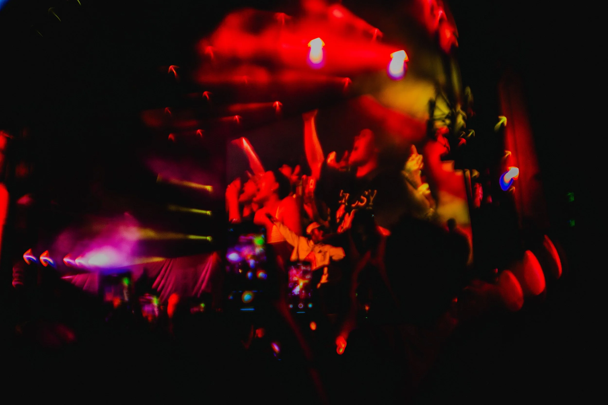 A concert scene with people dancing and enjoying vibrant red, purple, and yellow lights, and a large video screen displaying abstract visuals.