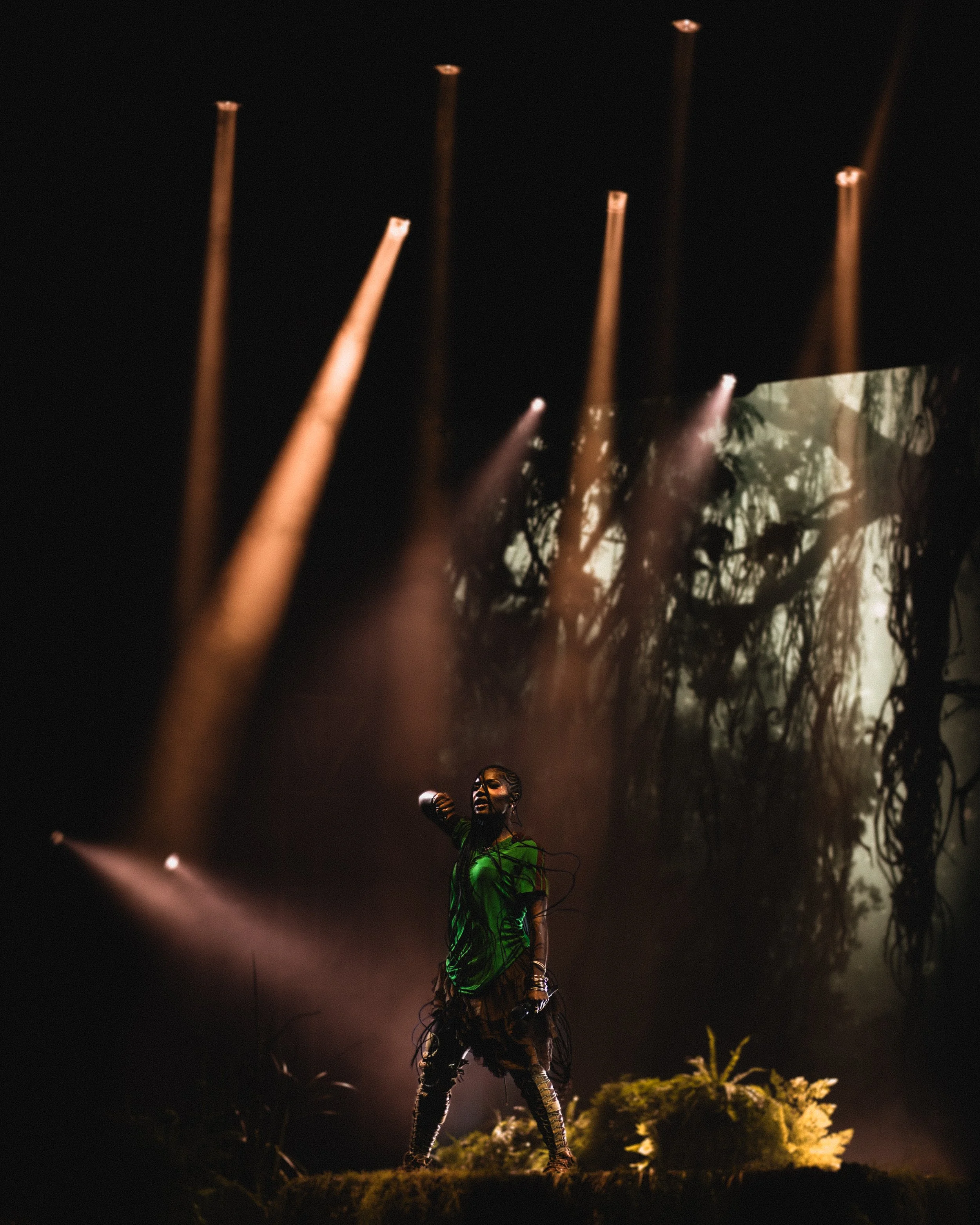 Performer singing on stage with jungle-themed backdrop and dramatic lighting.