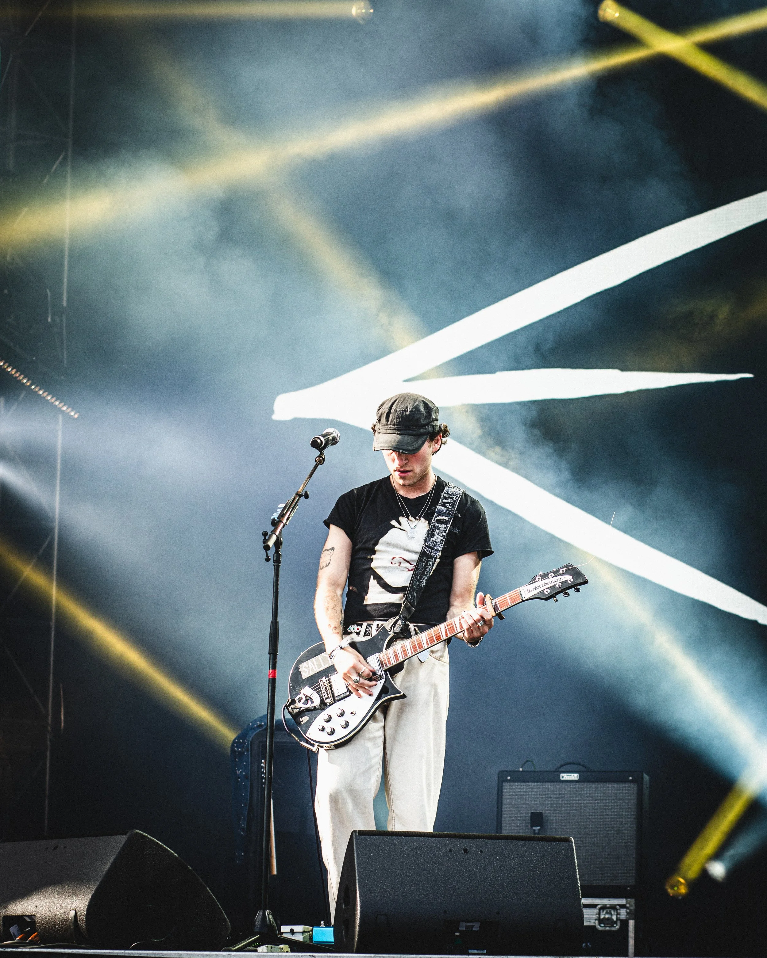 A male musician playing an electric guitar on stage with colorful lights and background visuals.