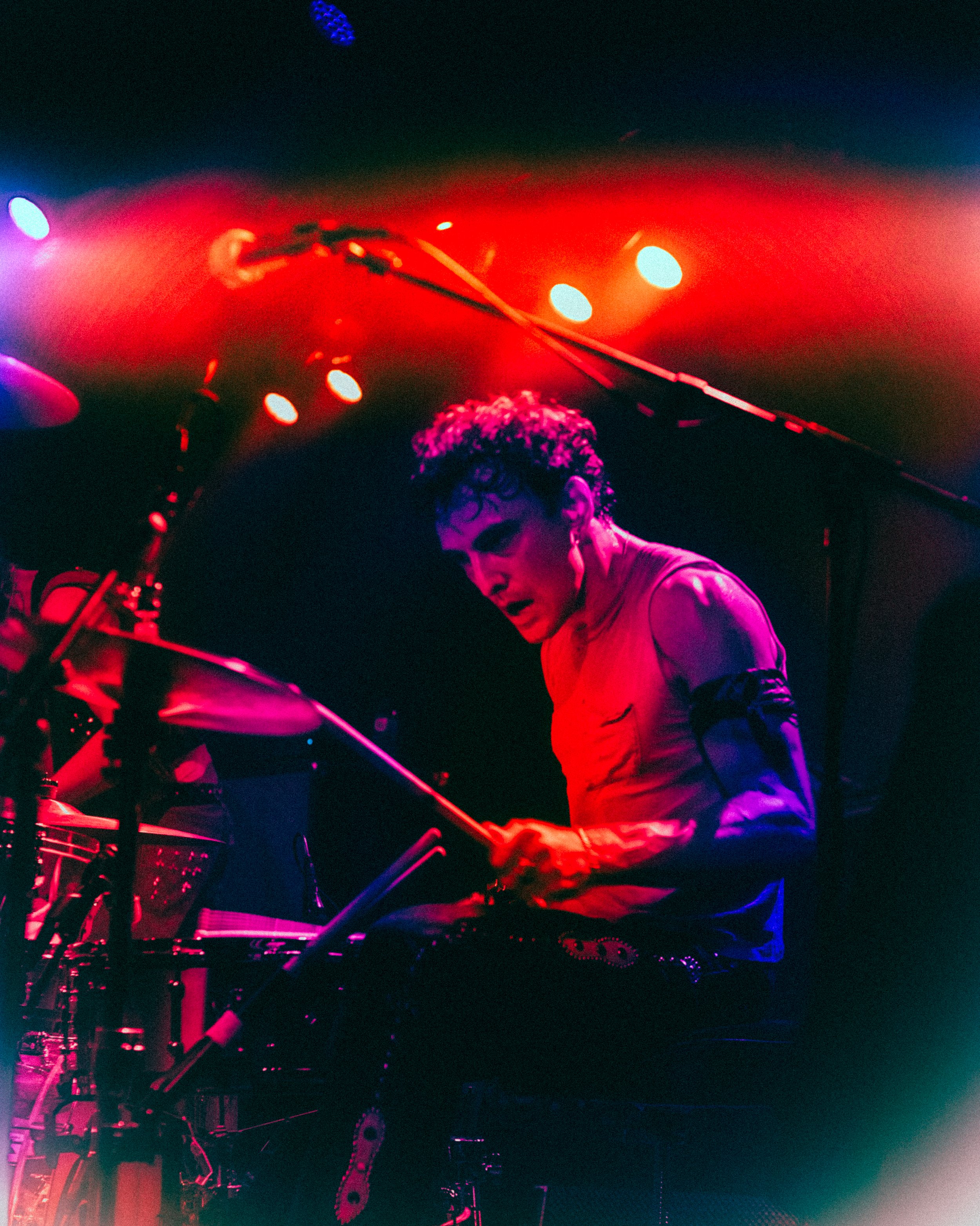 A musician playing the drums on stage under colorful lights.
